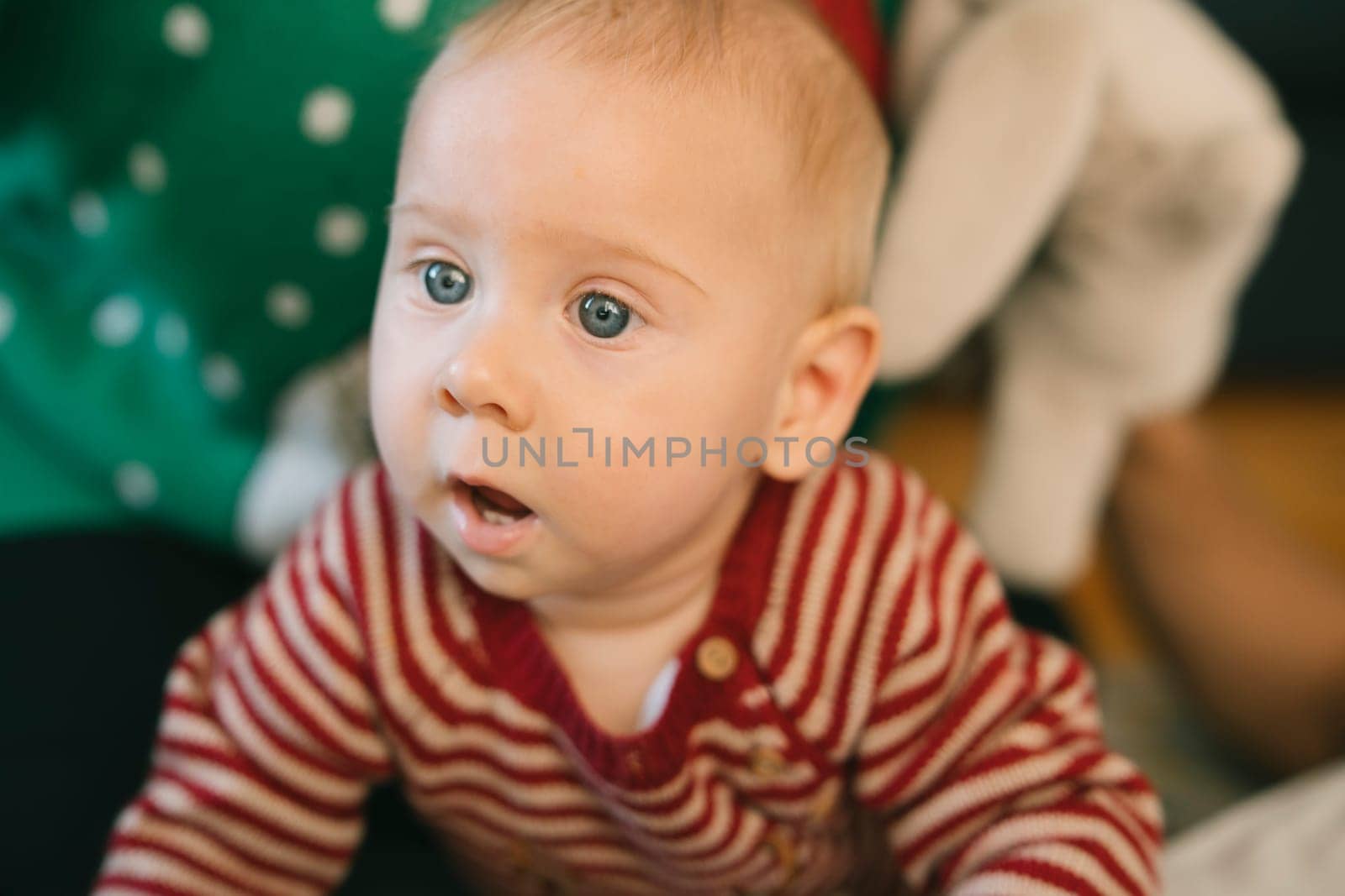A closeup of a curious baby with blue eyes, dressed in colorful stripes, surrounded by warmth and joy