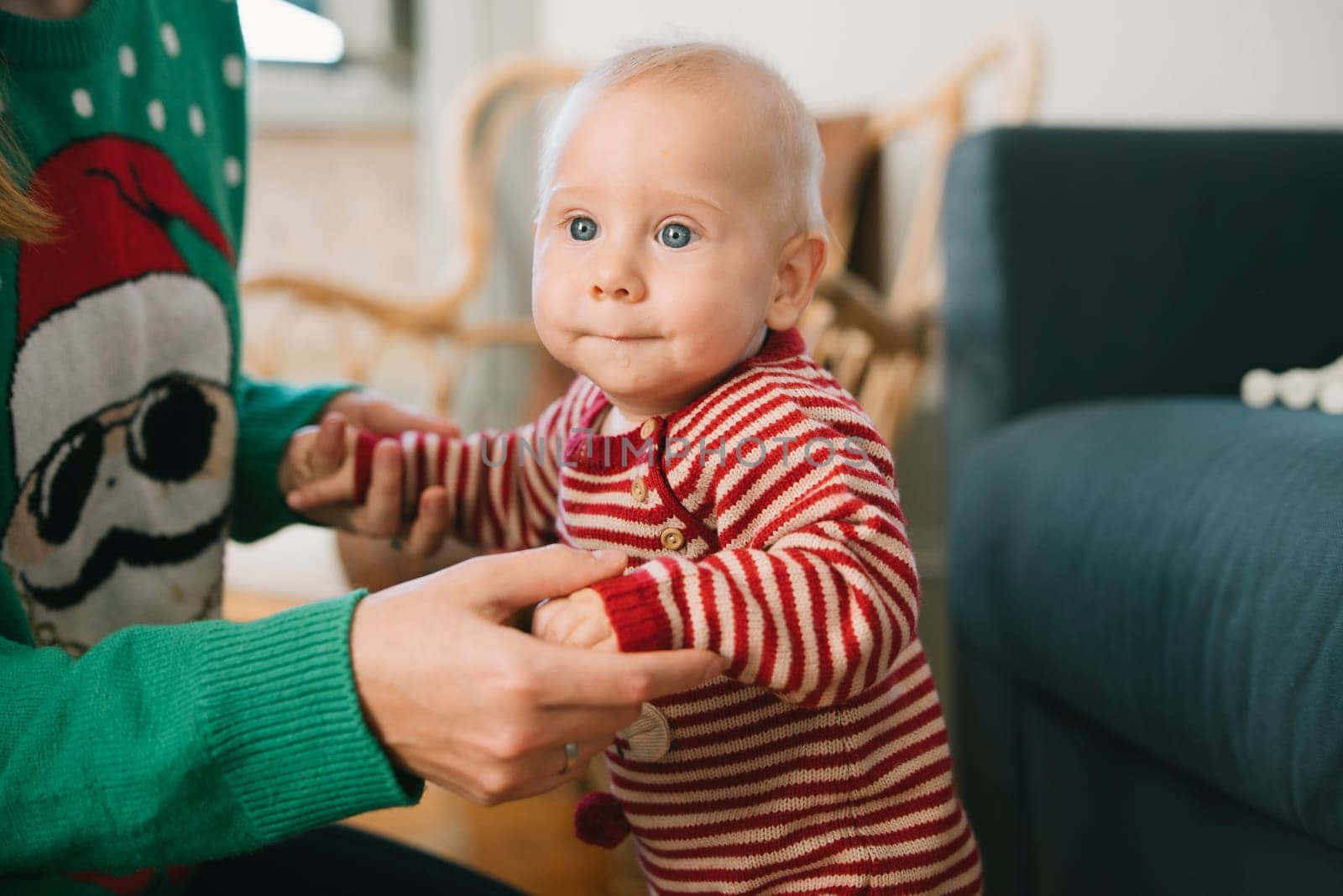 A charming little baby, dressed up for the festive holidays, learns to stand with support in a cozy home setting