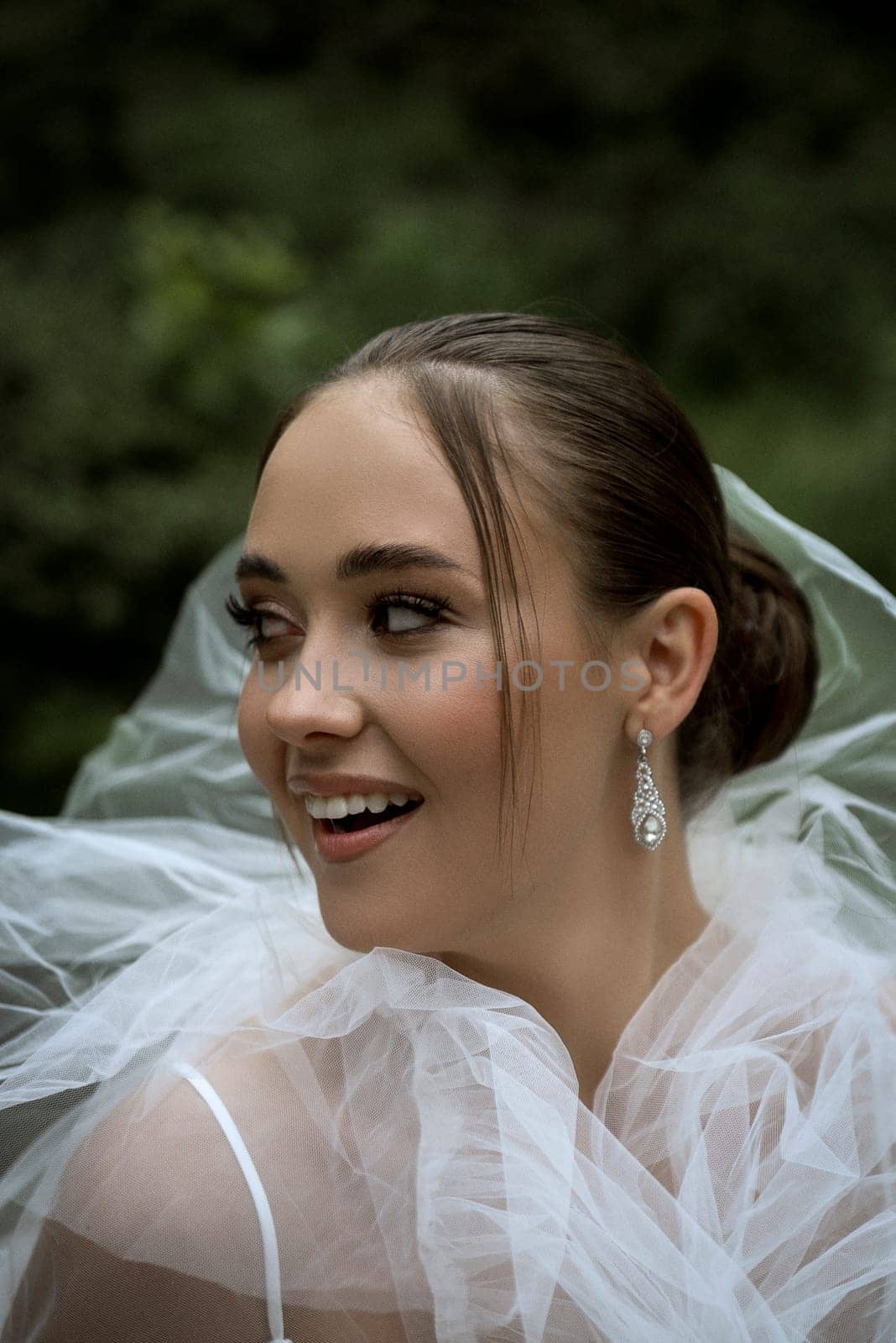 close-up of a bride covered with a white veil. beautiful brunette girl with a smooth hairstyle and stylish makeup. folds of an elegant, white veil around the girl's face, the bride looks away