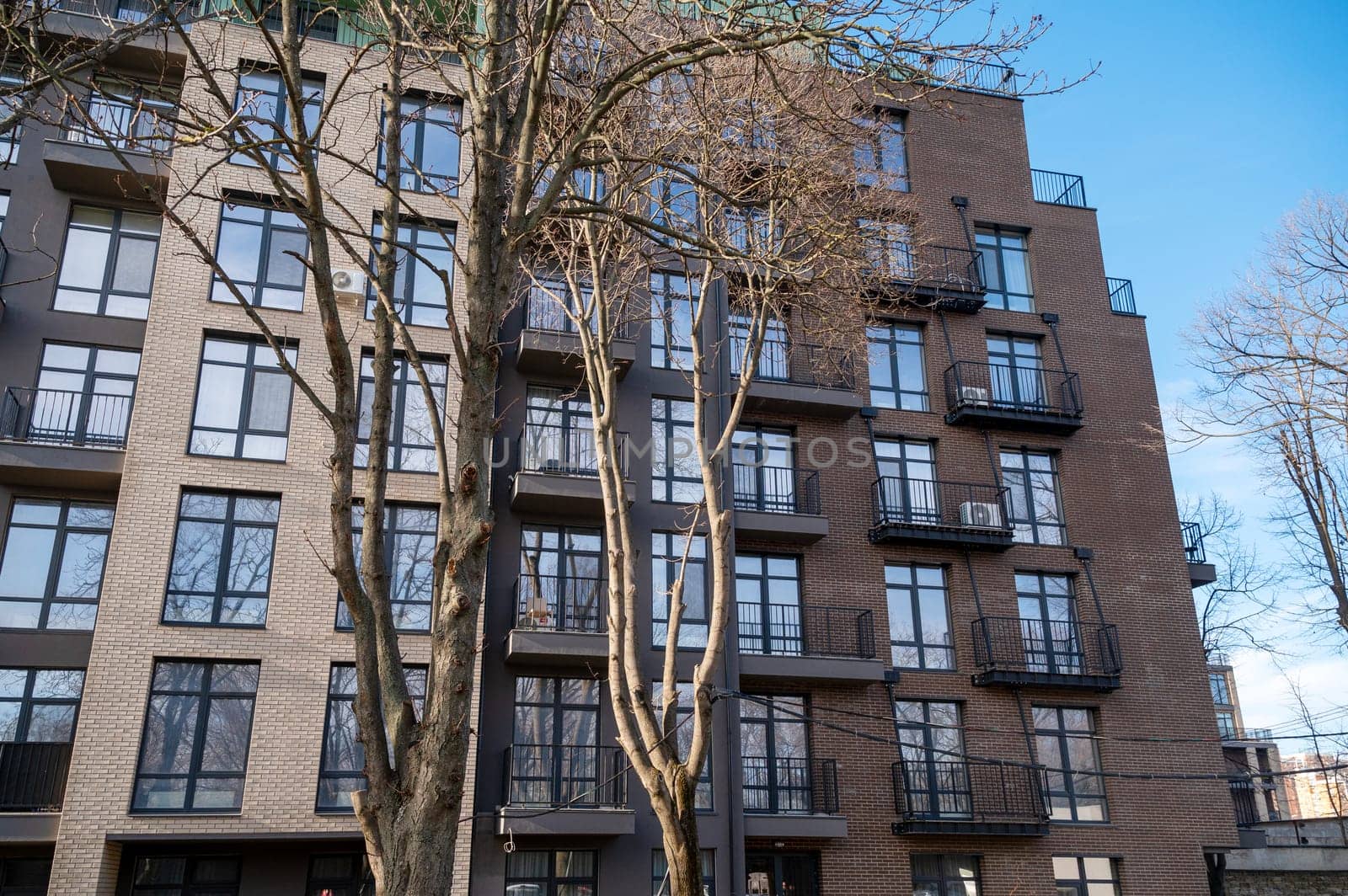 A tall building. High quality photo, Multi-storey new house with energy-saving facade. Brown wall with light stripes. Autumn trees in front of the house.