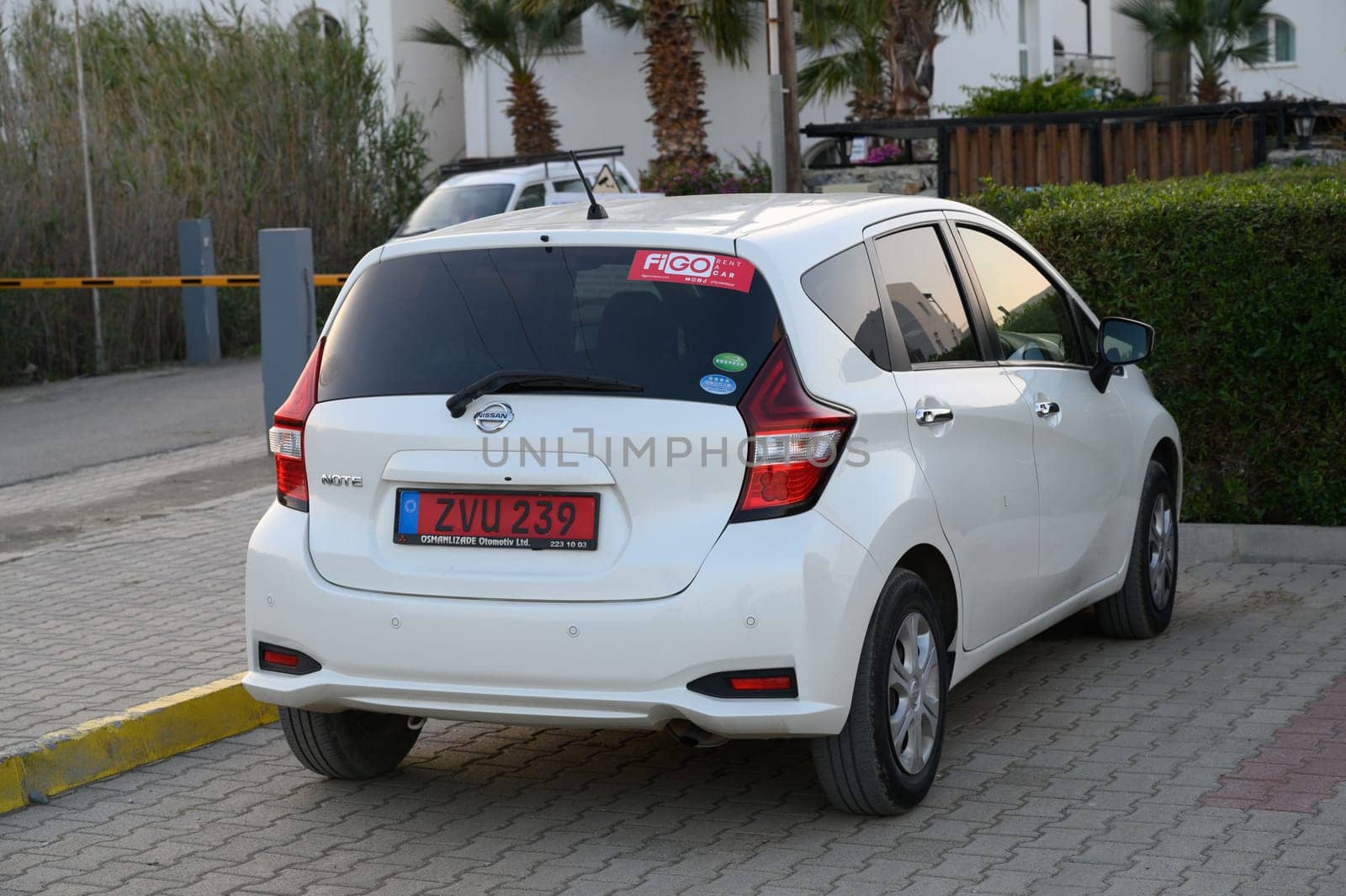 Gaziveren Cyprus -30.01.2025 A small white car is parked in a serene environment, embraced by lush greenery and swaying palm trees at dusk.