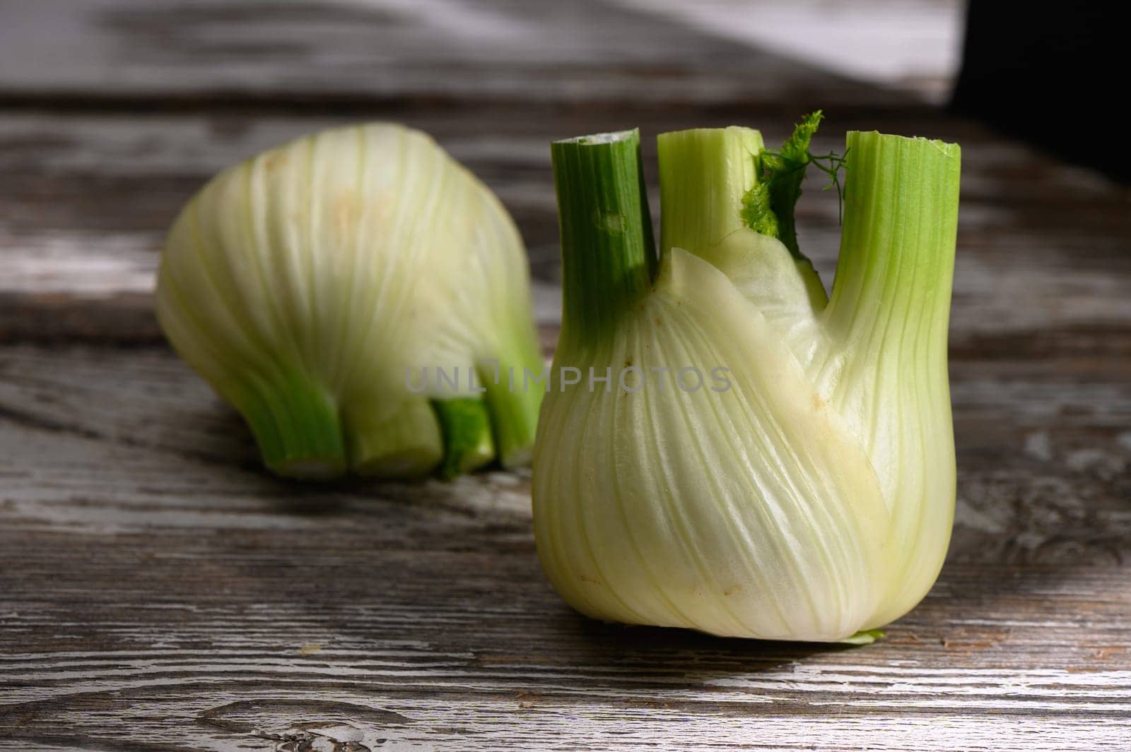Sliced fennel bulbs rest on an old wooden table, illuminated by gentle afternoon light, highlighting their freshness.
