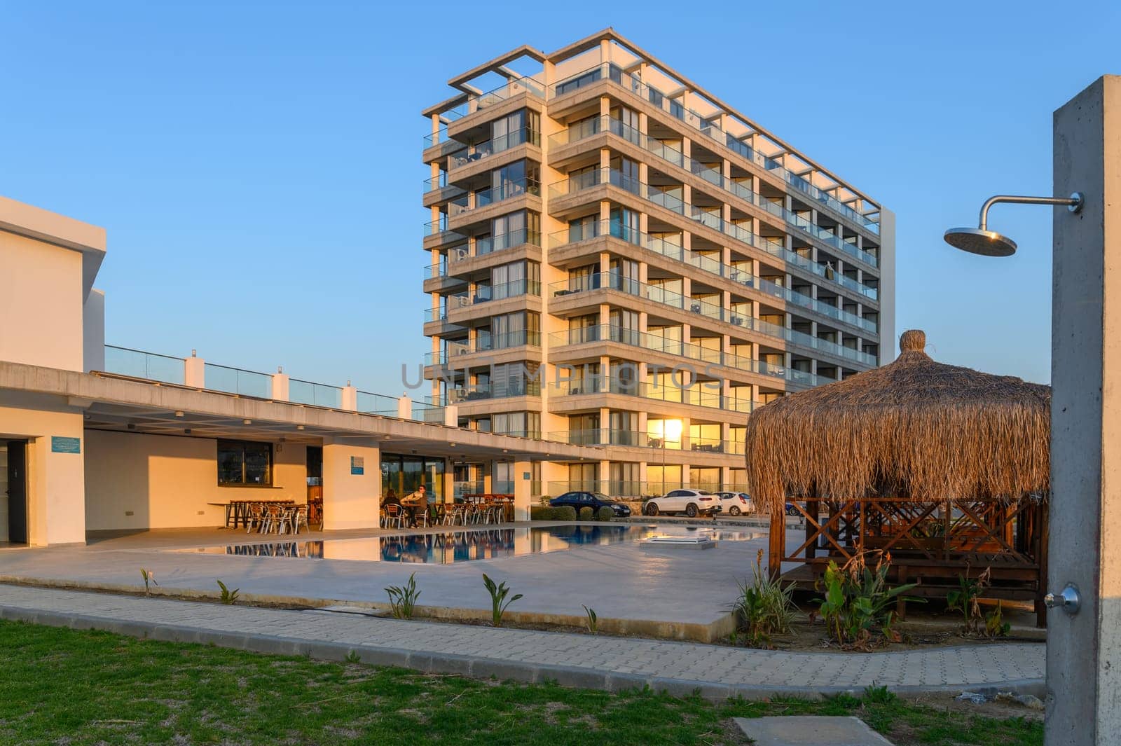 A sleek resort building stands beside a tranquil pool, reflecting golden sunlight in the evening.