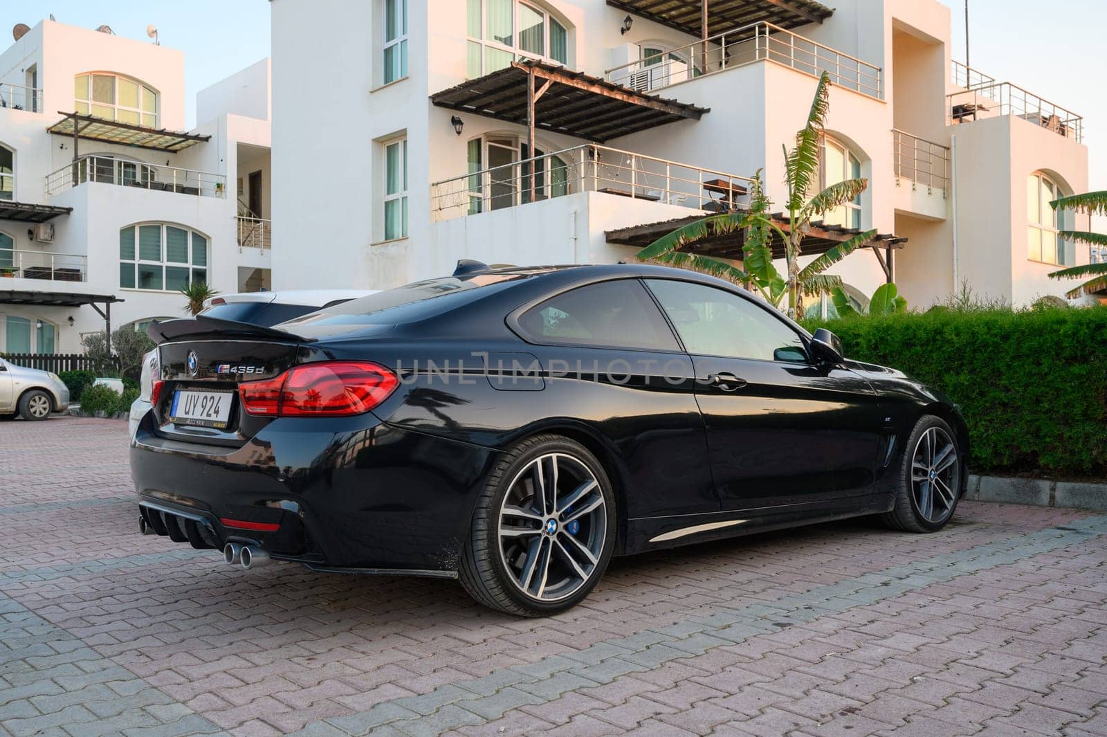 Gaziveren Cyprus -30.01.2025 A stylish black coupe rests quietly in front of a contemporary building, bathed in warm evening sunlight.
