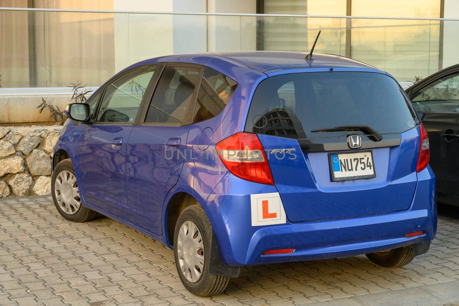 Gaziveren Cyprus -30.01.2025 A compact blue vehicle with a learner's permit sticker stands parked in a bustling urban area during sunset.