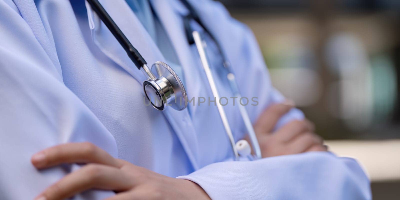 Close up of a doctor arms crossed, wearing a white coat and stethoscope, representing professionalism and commitment in the medical field.