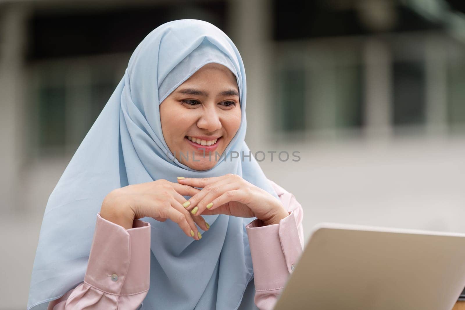 A happy Muslim woman in a hijab focuses on her laptop, showcasing enthusiasm and dedication in her professional endeavors.