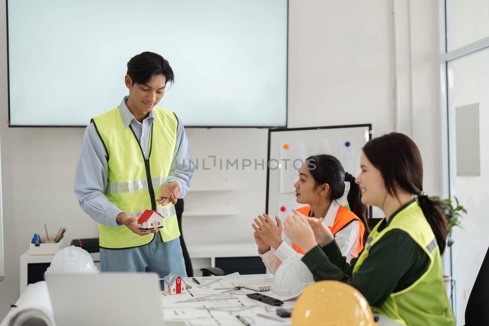 A diverse construction team enthusiastically applauding a colleague presenting a miniature building model, showcasing teamwork in a vibrant modern office.