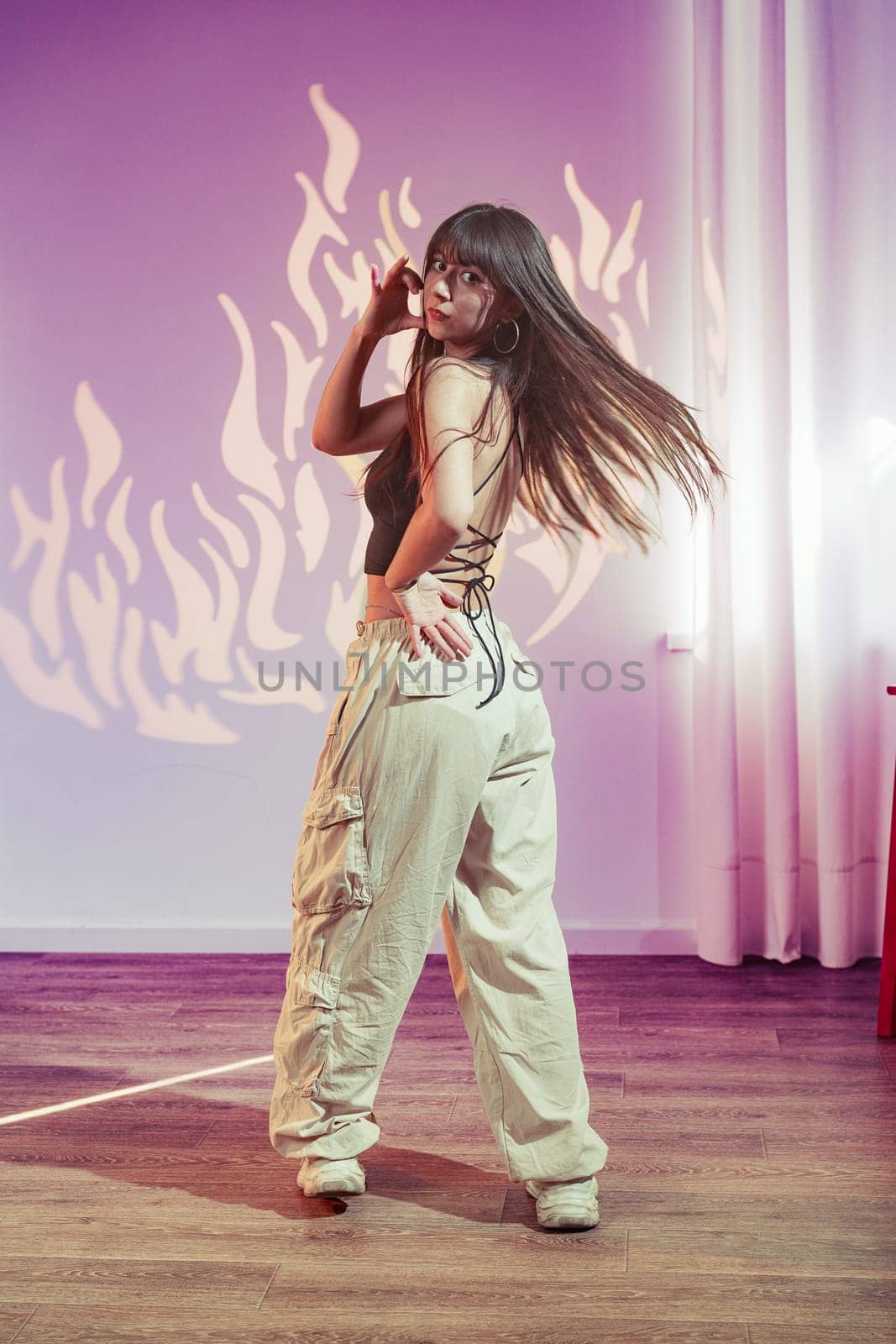 A young woman stands gracefully, showcasing a trendy outfit with baggy pants. The interesting background features vibrant flame patterns, enhancing her dynamic pose.