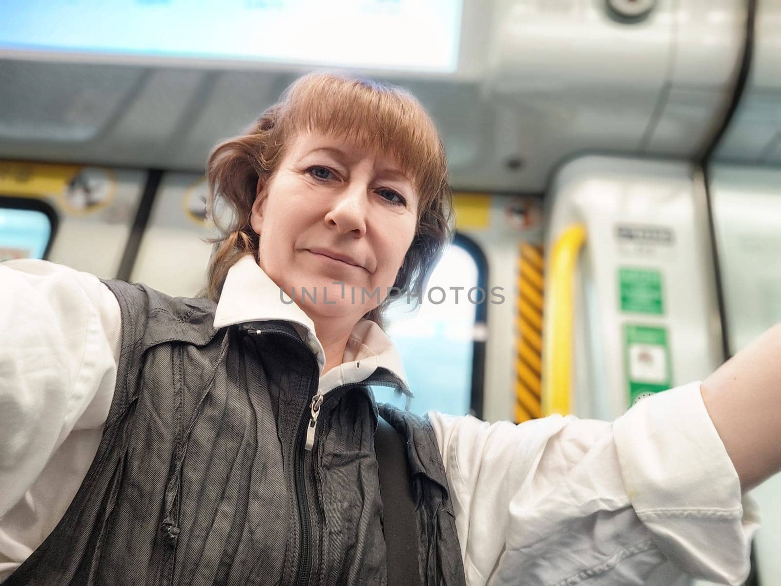 Middle-aged woman takes a selfie while traveling on the subway in Hong Kong, enjoying her urban exploration and local culture.
