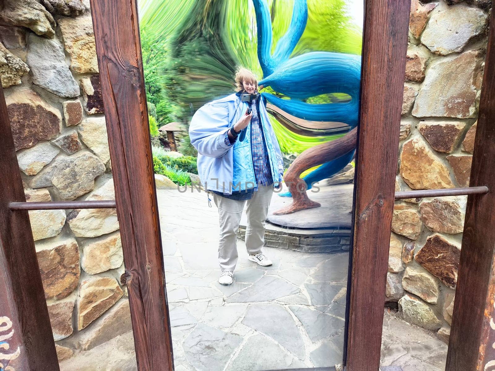A modern woman captures a humorous selfie in a warped mirror while exploring a scenic park on her journey.