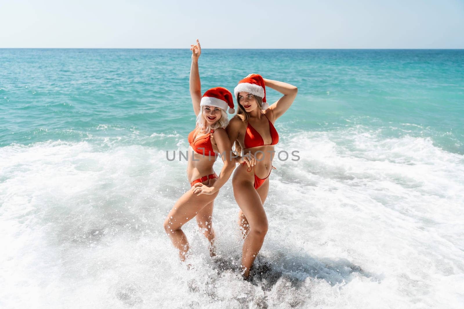 Women in Santa Claus hats run into the sea dressed in red swimsuits. Celebrating the New Year in a hot country.