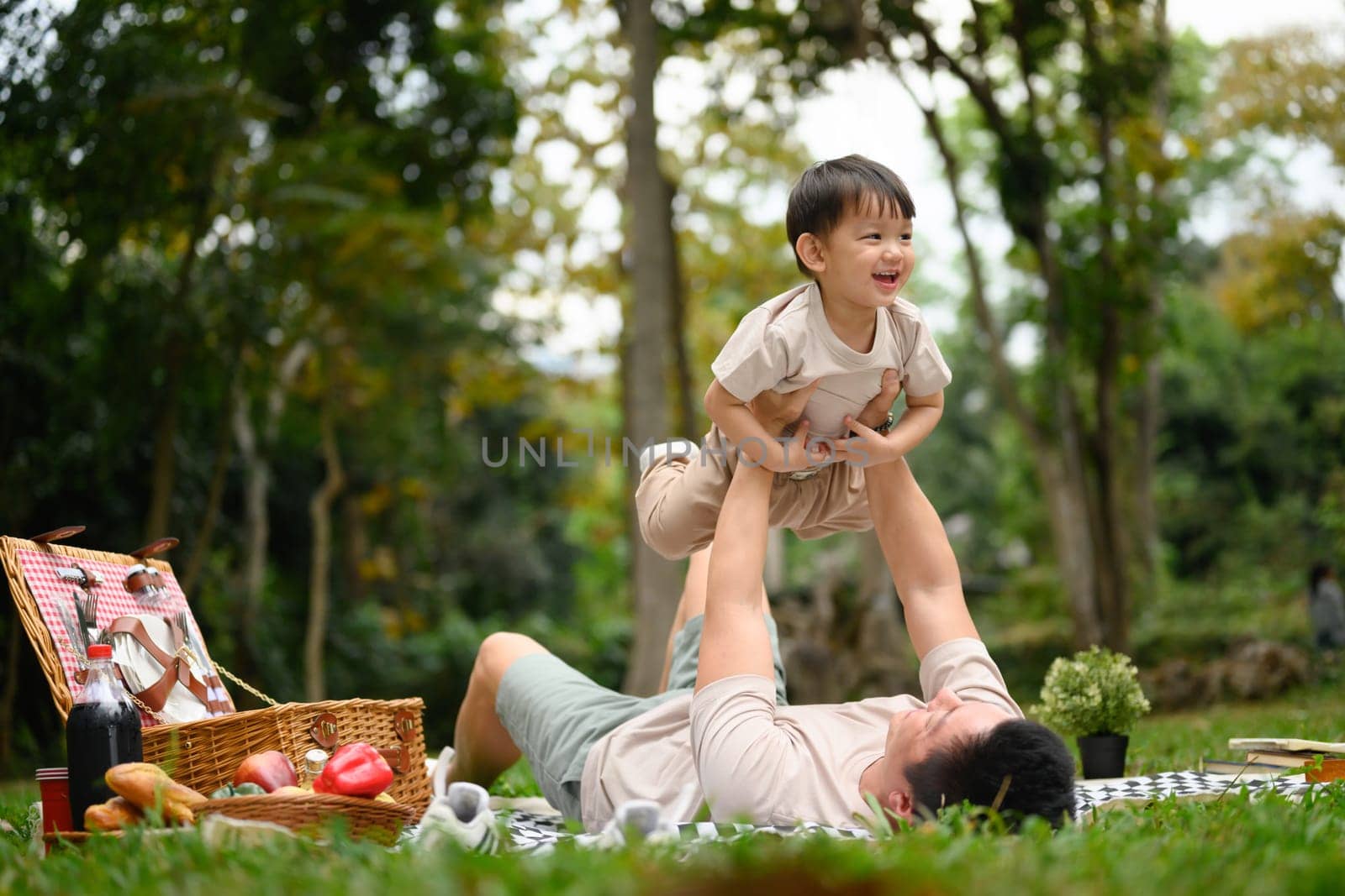 Father and little son on playing during a picnic in a lush green park.