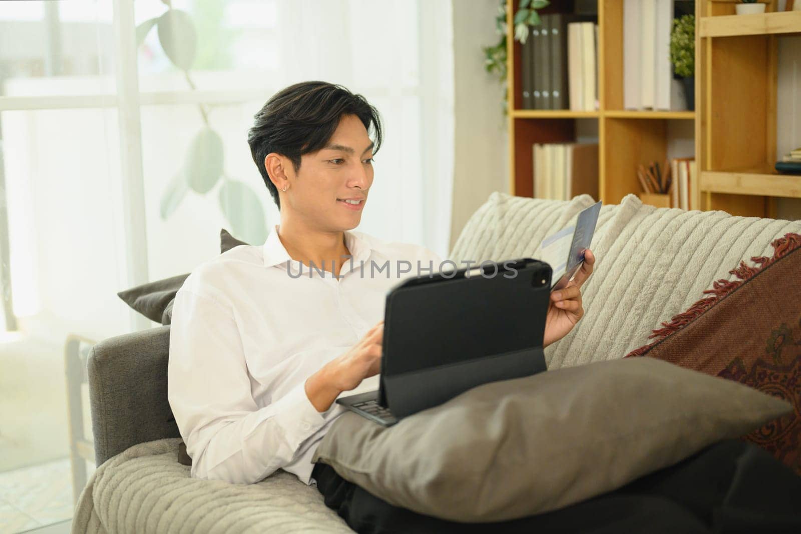 Smiling asian man holding a savings passbook and checking his financial transactions on digital tablet.