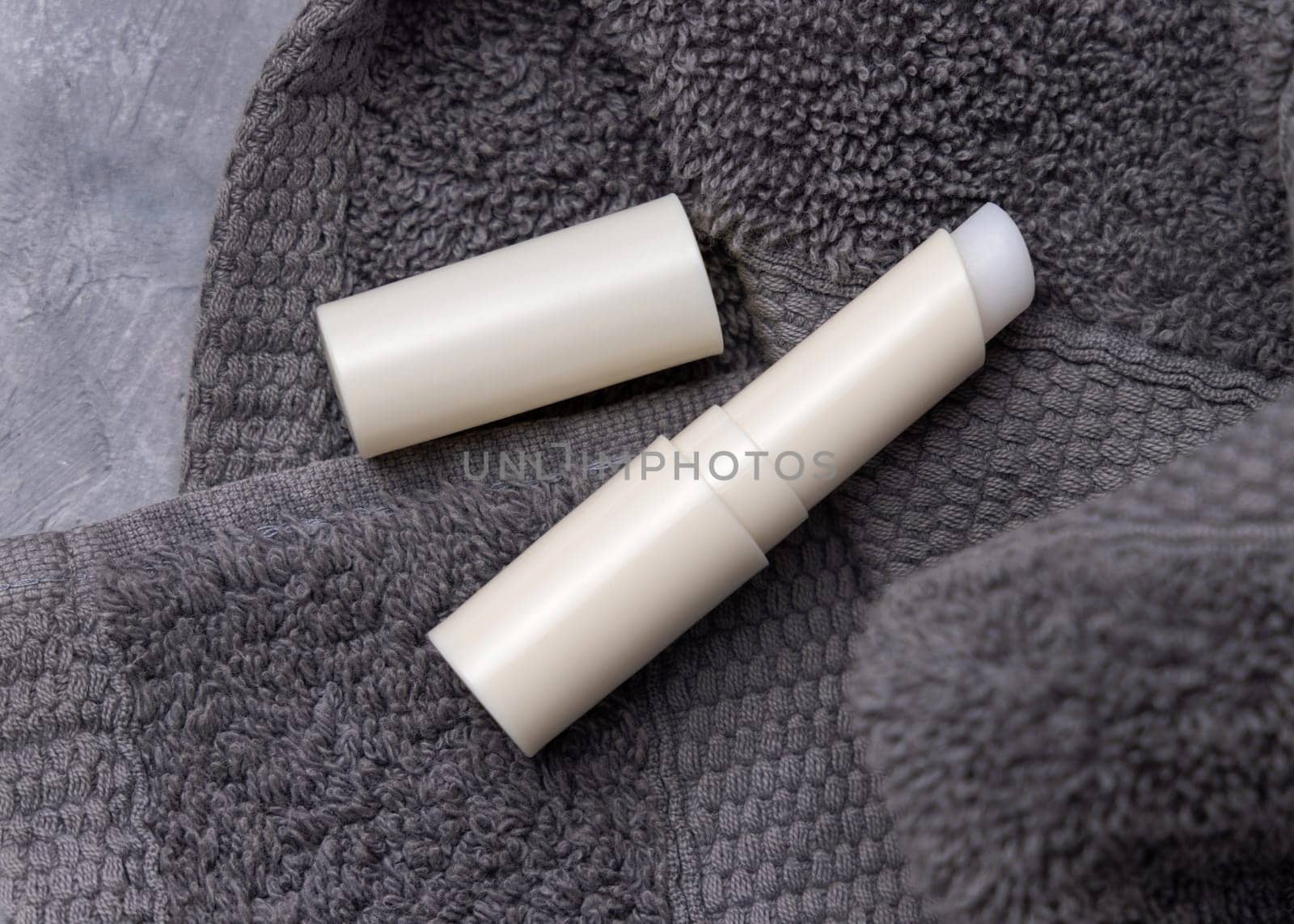 Opened white blank lip balm stick on dark grey folded towels top view, cosmetic packaging mockup, copy space. Lipcare beauty product for mens everyday personal care