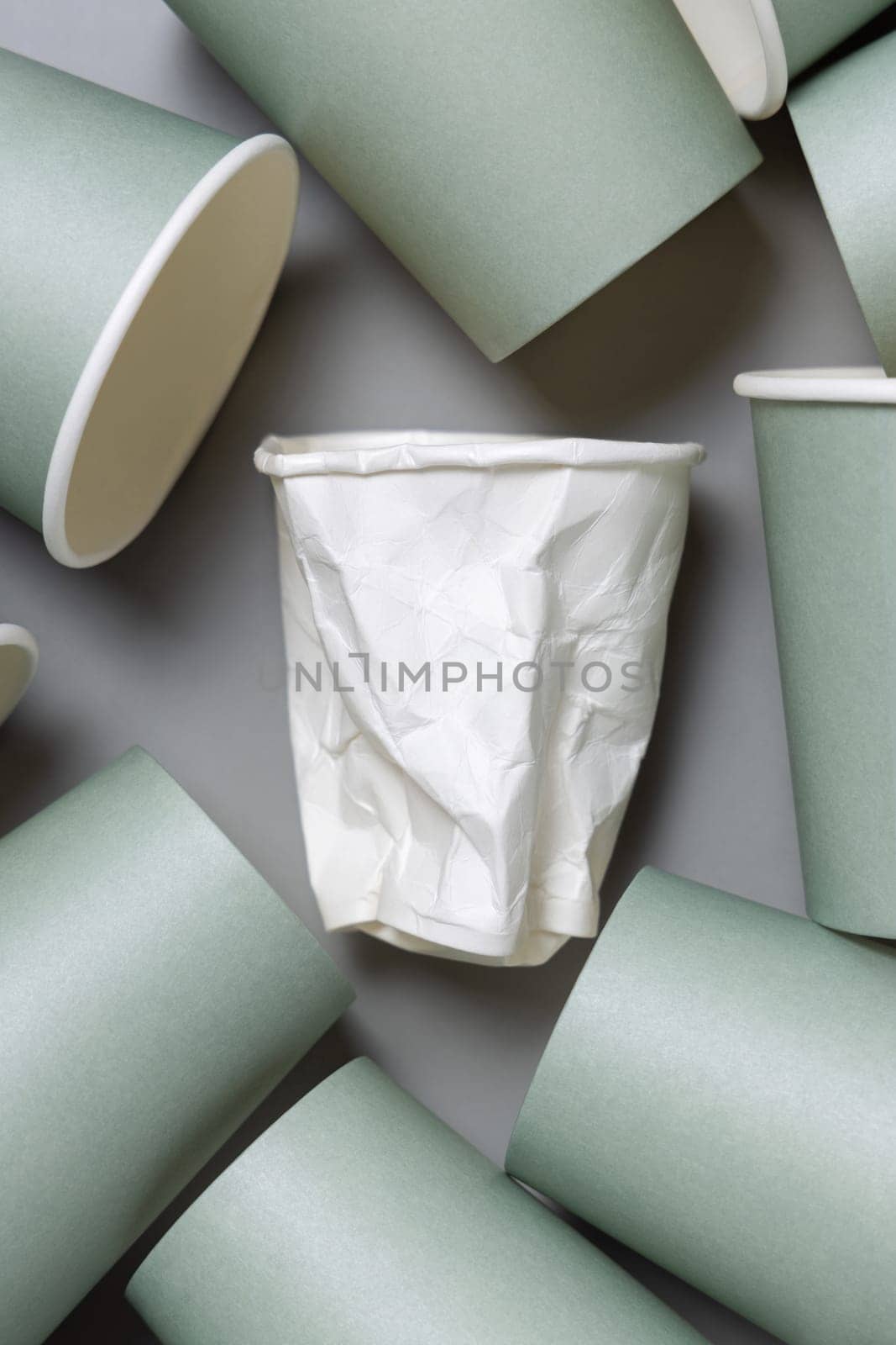 Disposable new light green paper cups and crumpled used white one on gray top view, mockup with copy space. Empty cardboard coffee cups flat lay. Consumerism concept
