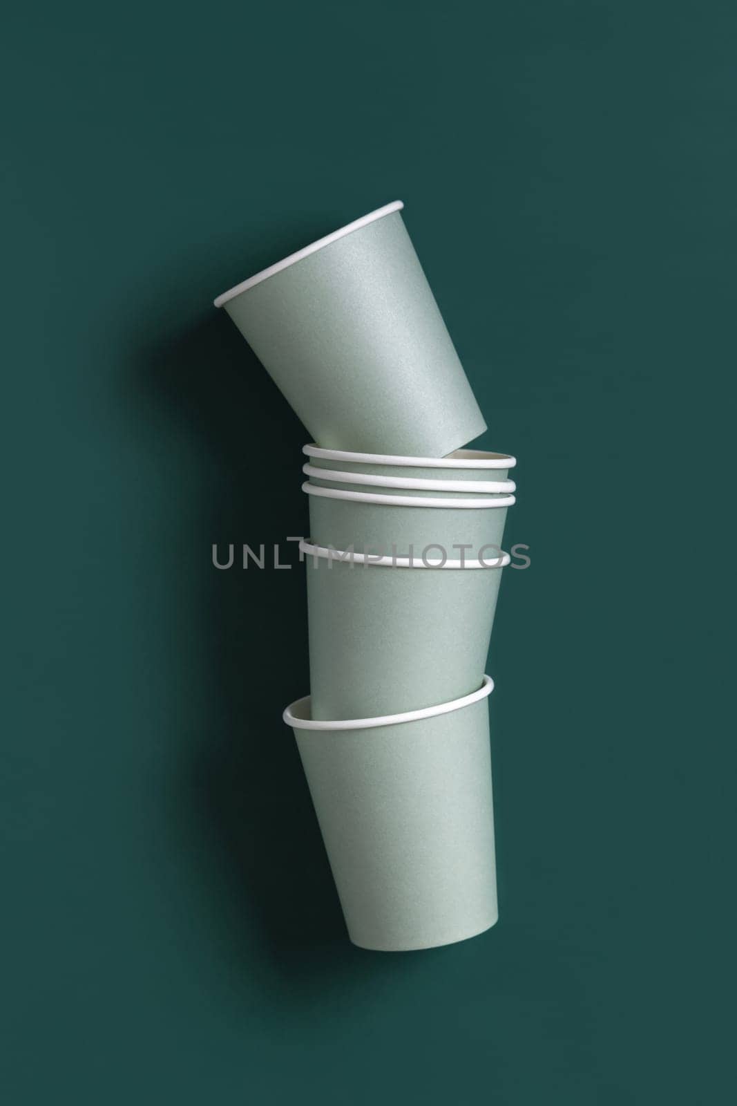 Disposable light green paper cups on a dark green background top view, mockup with advertising copy space. Empty cardboard coffee cups flat lay. No plastic and sustainable lifestyle concept