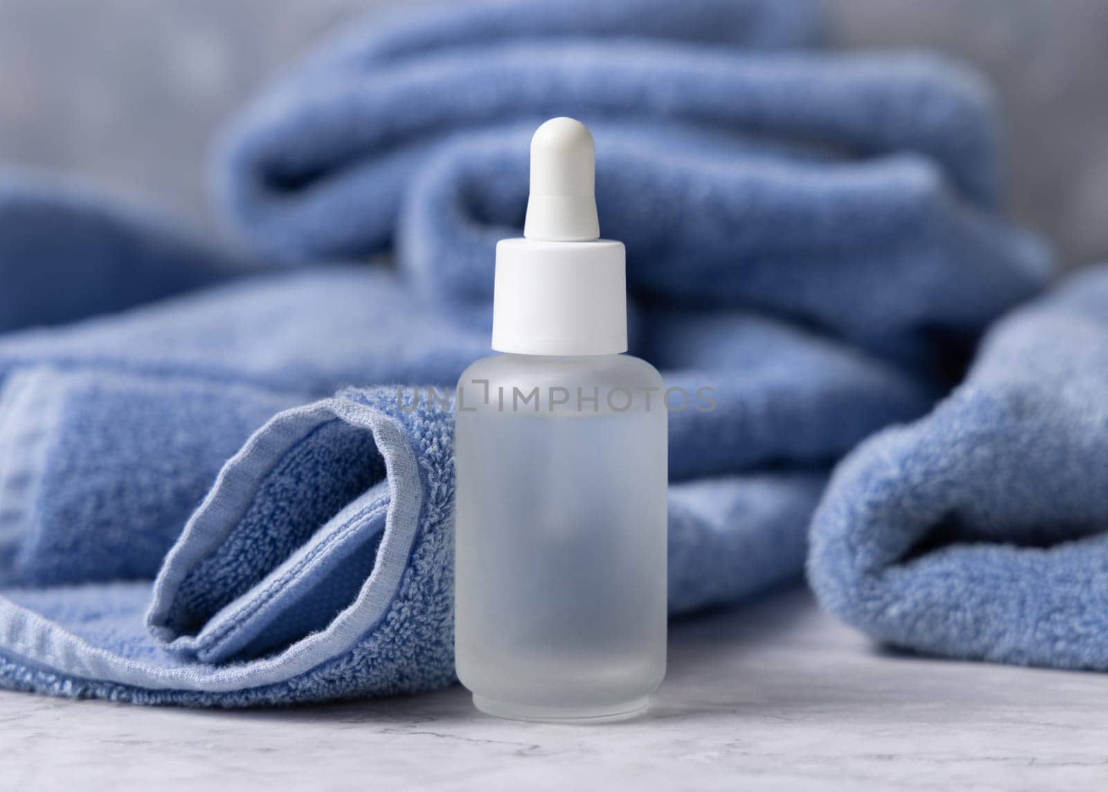 Clear glass dropper bottle with pipette near blue towel closeup, brand packaging mockup, copy space. Natural handmade cosmetic product for facecare and spa procedures - serum or essence