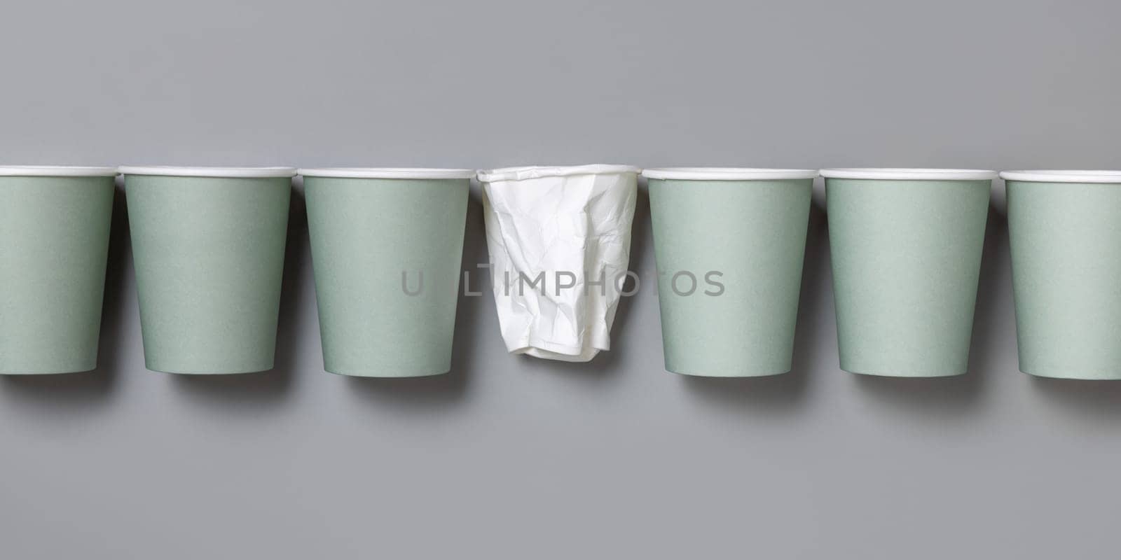 Disposable new light green paper cups and crumpled used white one in a line a gray top view, mockup with copy space. Empty cardboard coffee cups flat lay. No plastic and sustainable lifestyle concept