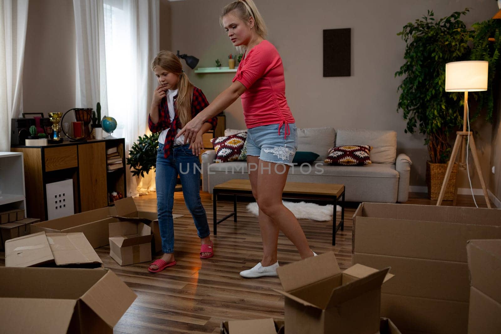 Two cheerful girls are joyfully unpacking various boxes in a bright, stylish living room that is filled with light