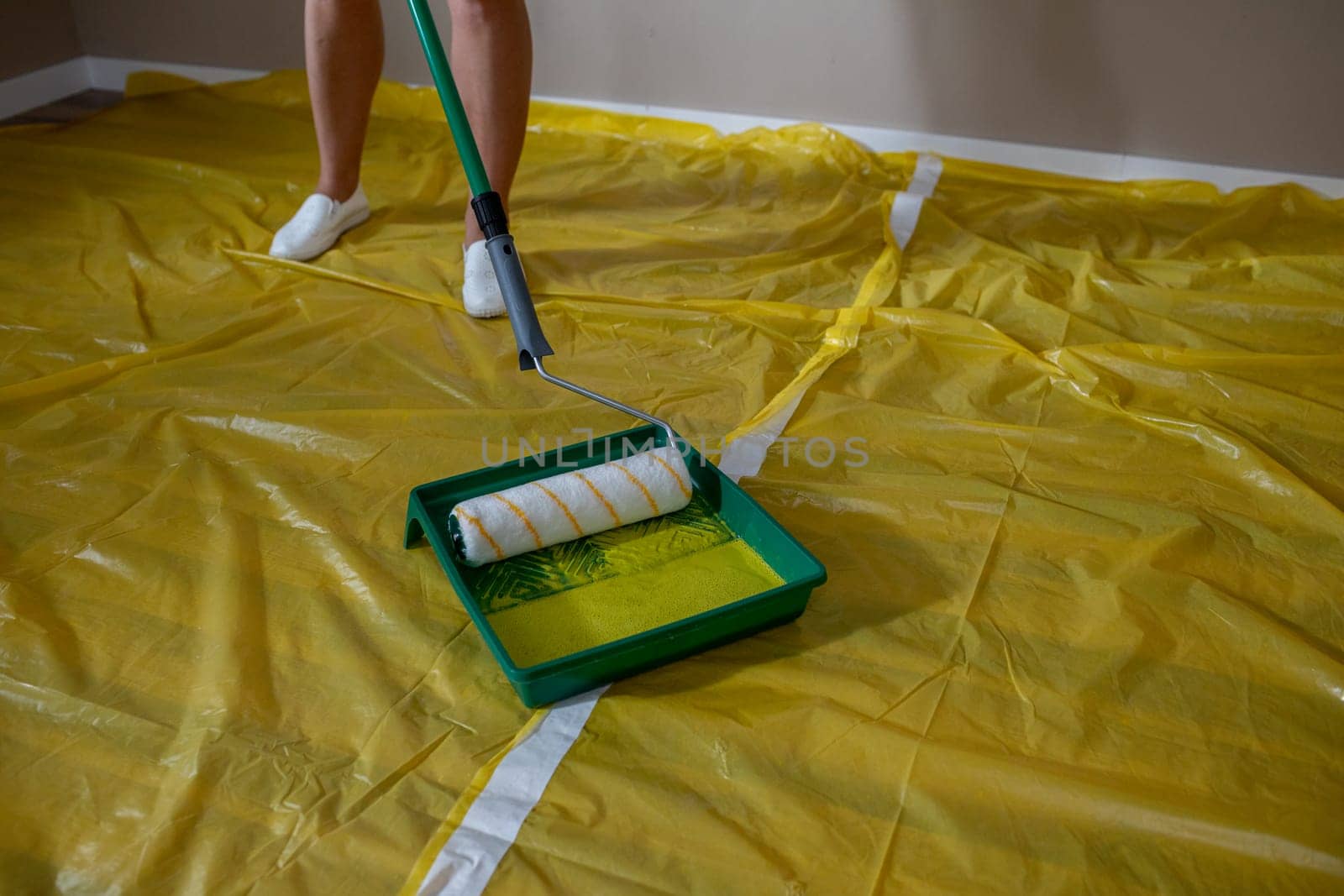 A person is meticulously painting a room with a roller while using a protective sheet laid out on the floor