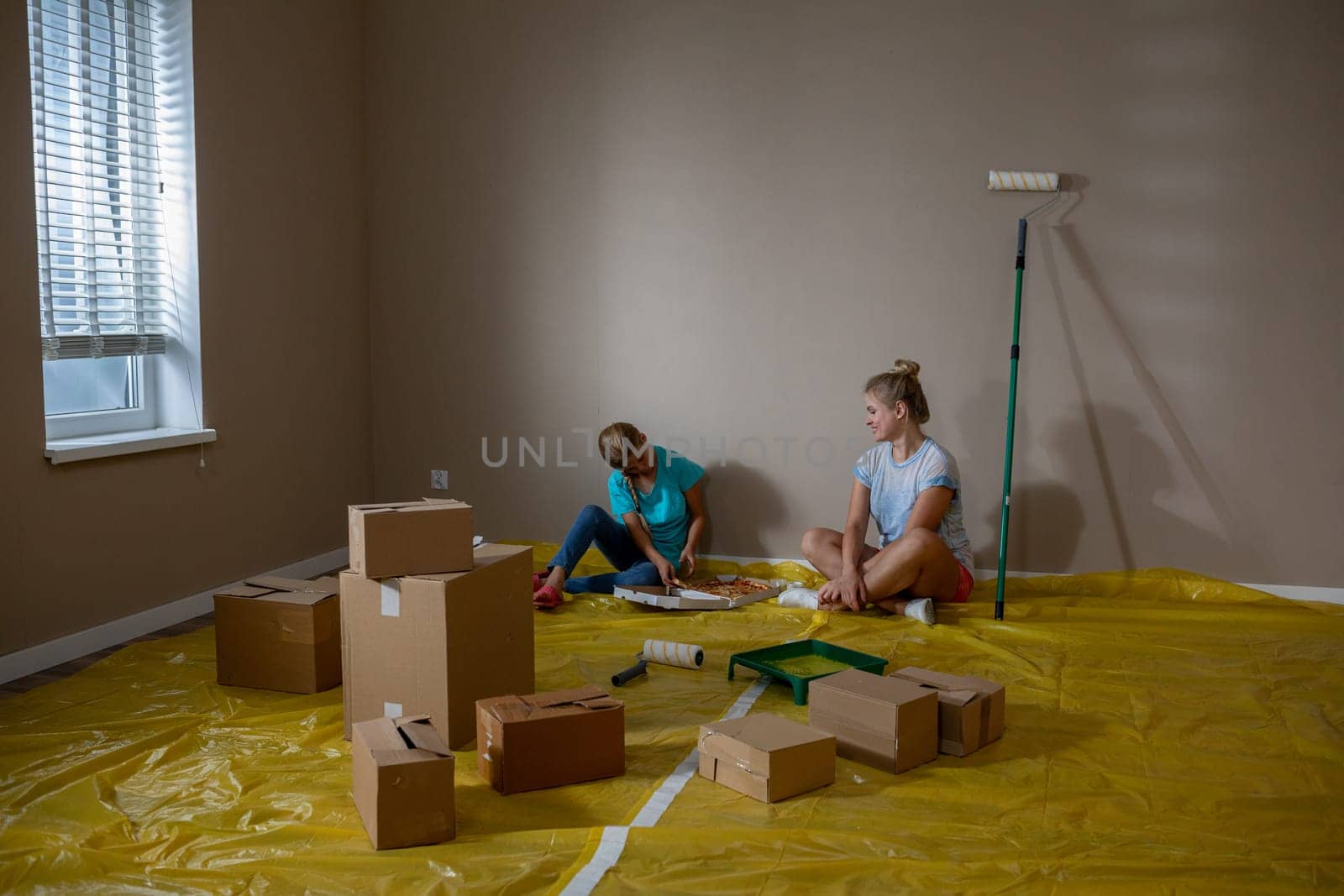 Two close friends actively engaged in a room renovation project, preparing to paint with supplies strewn around them
