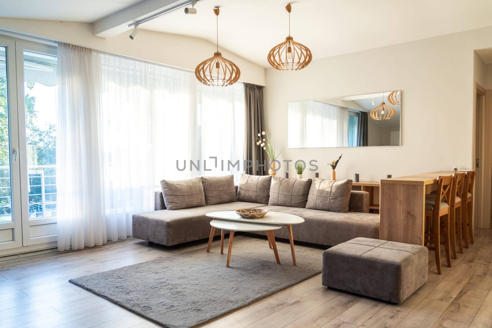 Bright modern living room with gray sectional sofa, white coffee table, wooden dining set, and large windows
