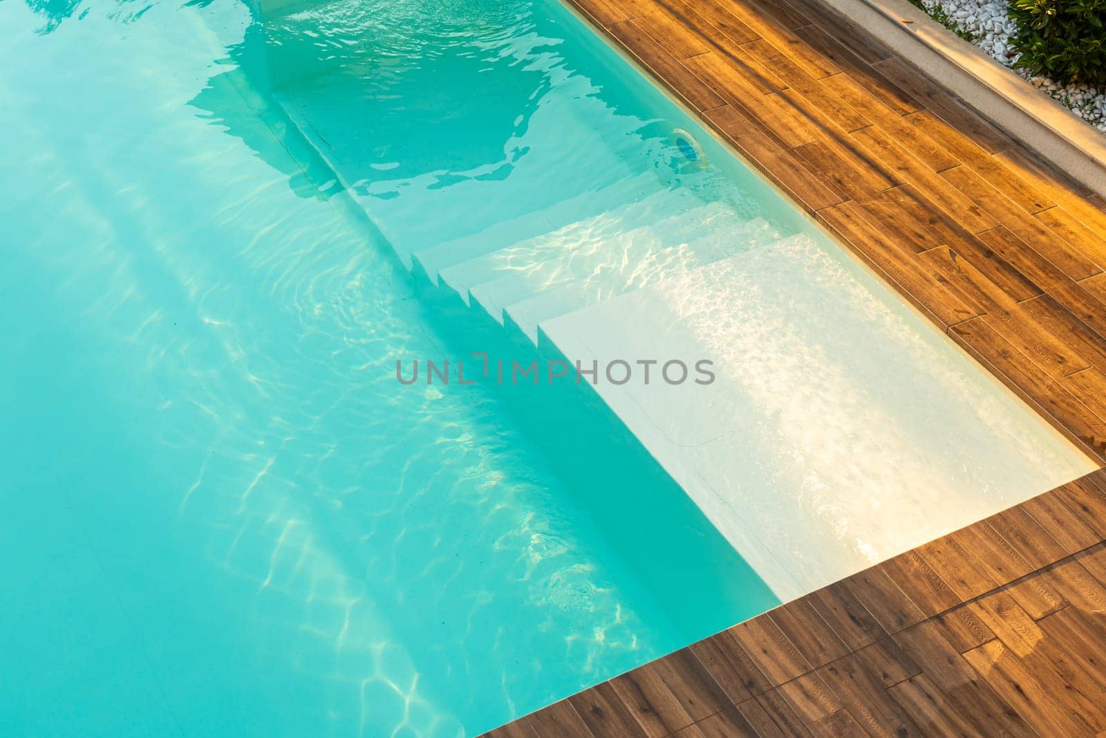 Turquoise swimming pool with elegant submerged steps and wooden deck in a serene outdoor setting