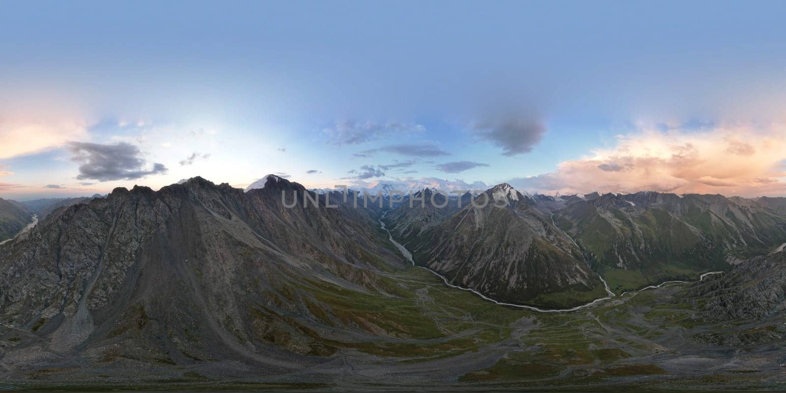 360 panorama of a mountainous area from a height. A drone view of sunrise in the mountains, orange clouds, snowy white mountain peaks, a green valley with river. Rocky terrain with cliffs. Khan Tengri