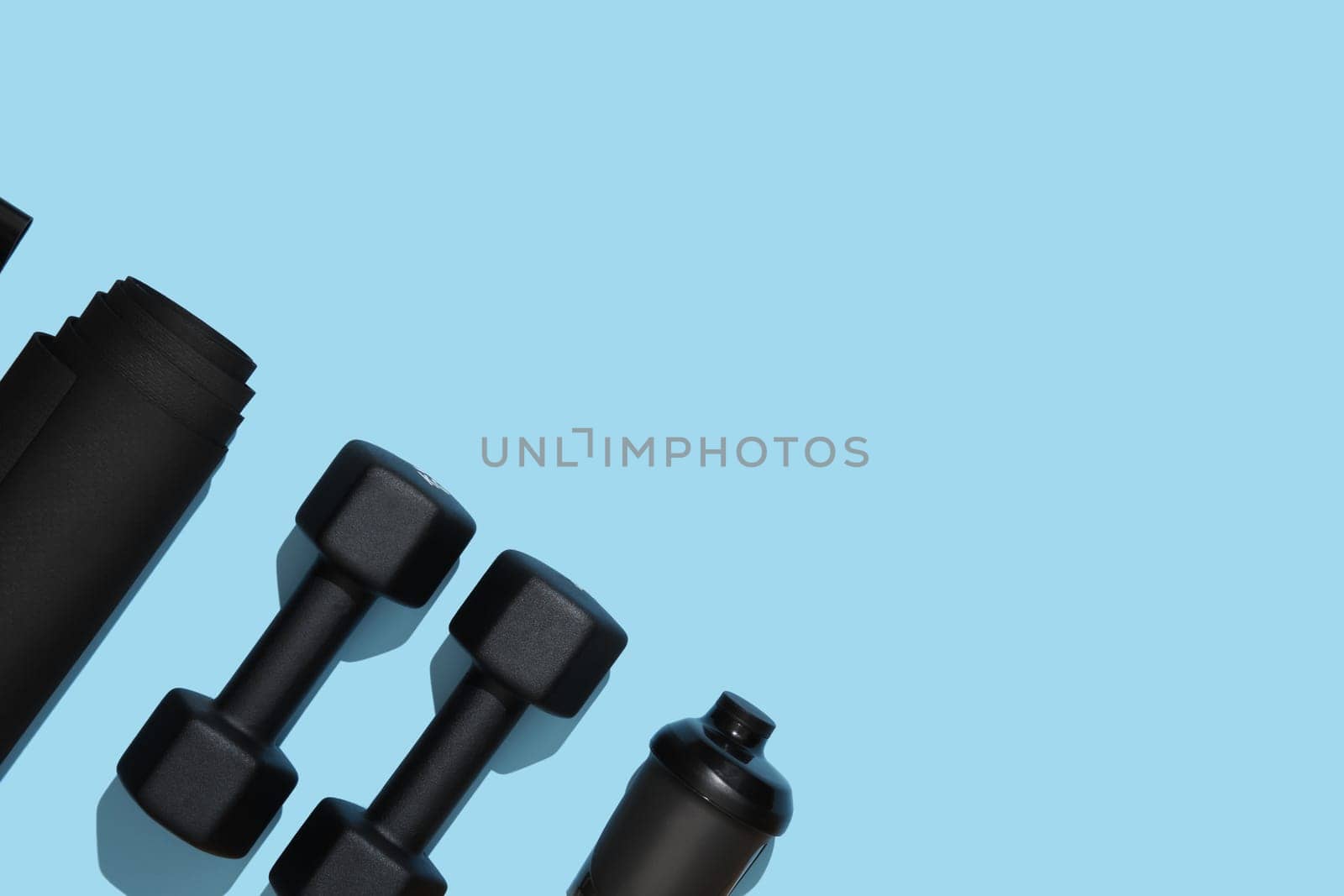 Black workout equipment, dumbbells, mat and water bottle on blue background. Fitness, sports items, healthy lifestyle concept. Place for your text