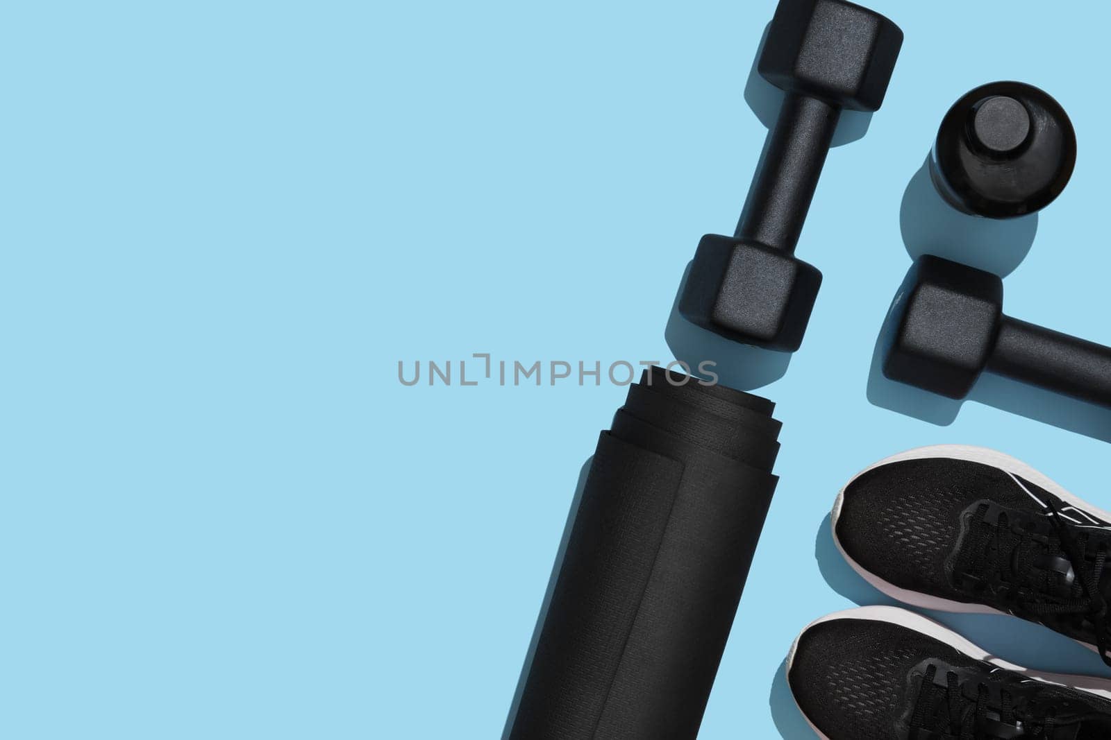 Black workout equipment, dumbbells, mat, sneakers and water bottle on blue background. Fitness, sports items, healthy lifestyle concept. Space for your text
