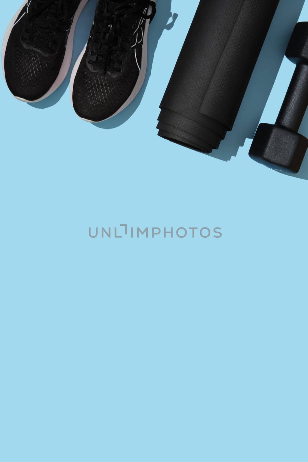 Vertical fitness background with black dumbbells, mat, sneakers on blue backdrop. Fitness, sports items, healthy lifestyle concept. Space for your text