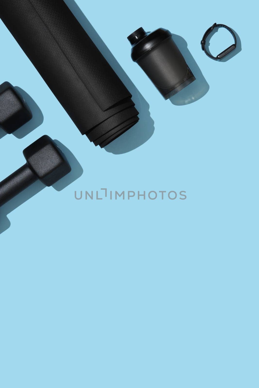 Vertical fitness banner with black dumbbells, mat, water bottle and fitness band on blue background. Fitness, sports items, healthy lifestyle concept. Space for your text