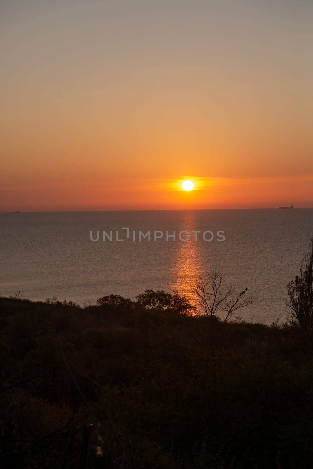 The bright sun rises over the sea. A ray of sun creates a path of warm light on the sea surface. The sea is calm, a golden sun is visible on the sea horizon, in the foreground are rocks.