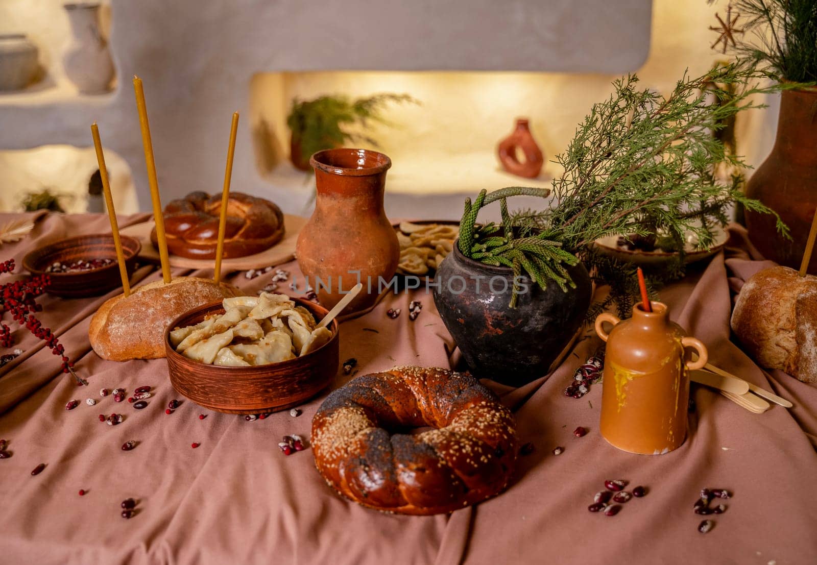 traditional table for a holiday. on the table close-up round bread, loaf, plate with dumplings, clay pot with ears of corn and pine branches. in the background wall with backlight