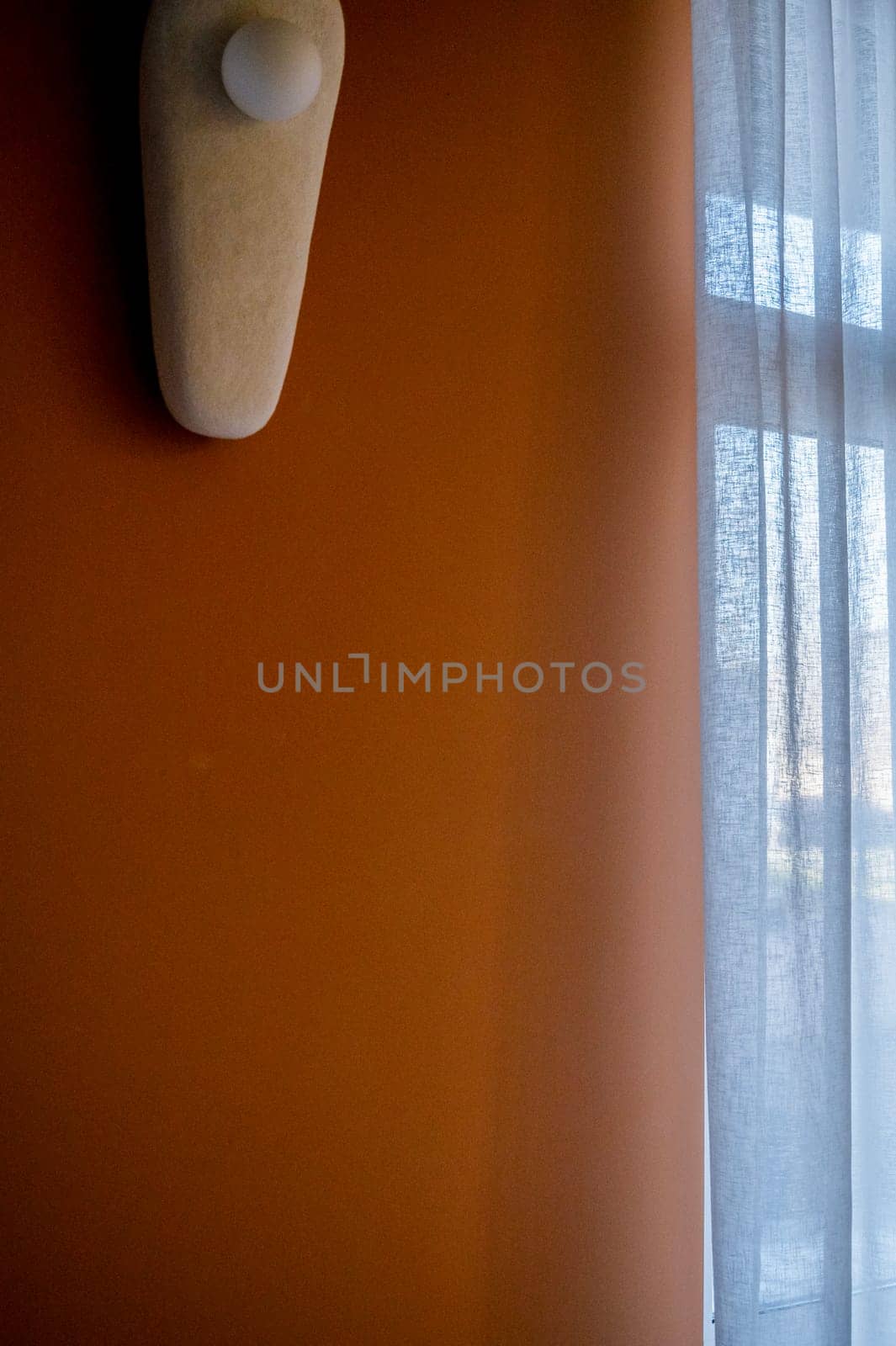a wall of rich beige color with a lamp. next to a large window. the lamp is oval, it hangs on the wall with ceramic elements.