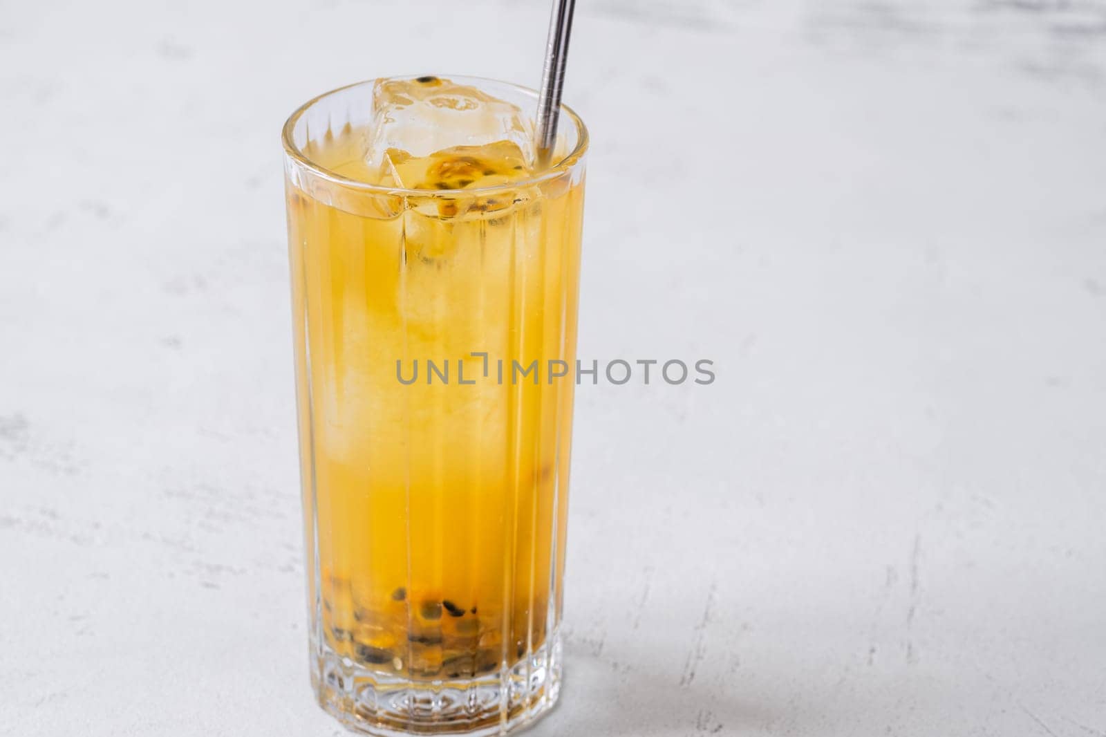 Passion Fruit Caipirinha cocktail in highball glass with straw on white wooden
