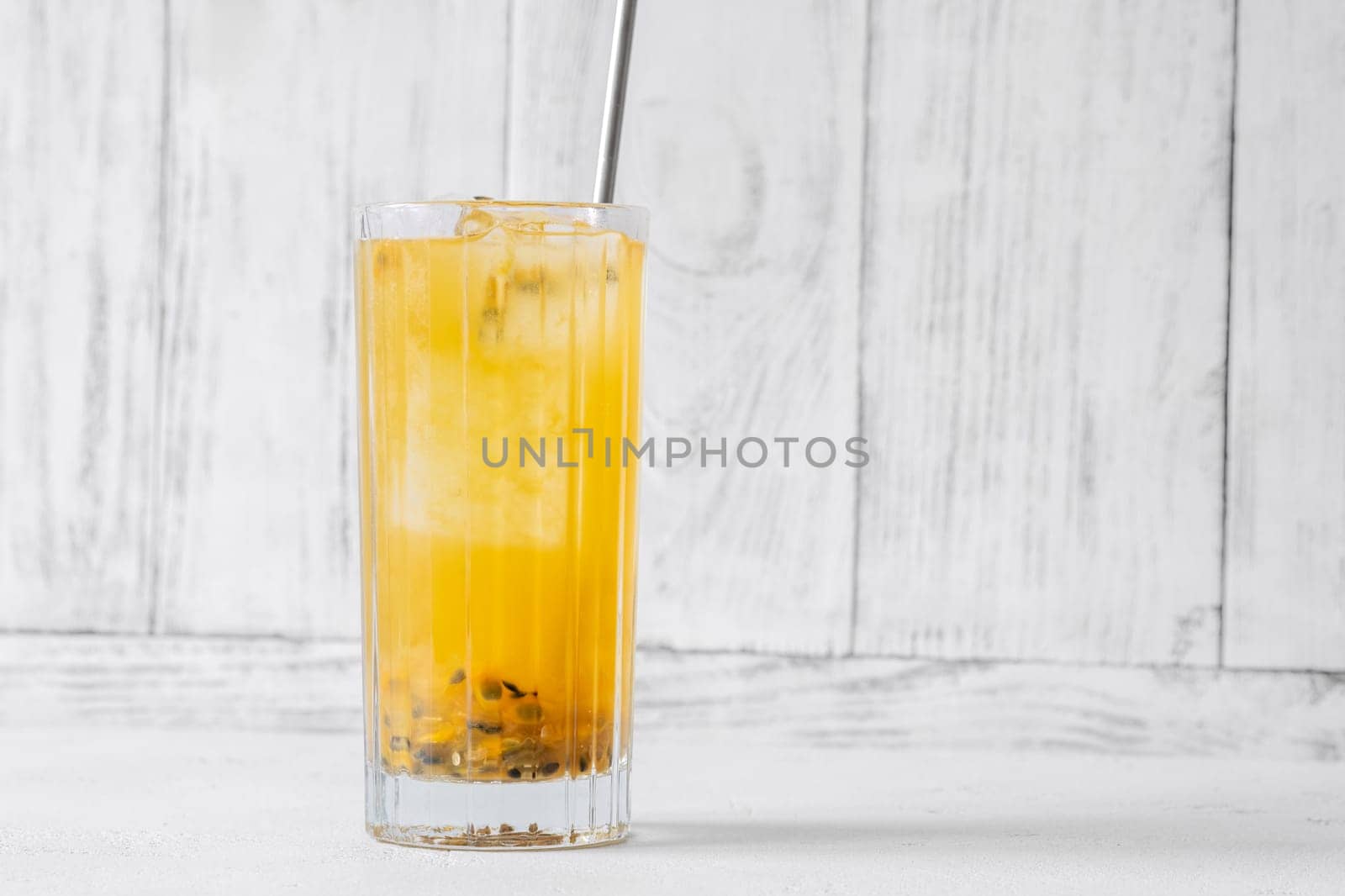 Passion Fruit Caipirinha cocktail in highball glass with straw on white wooden