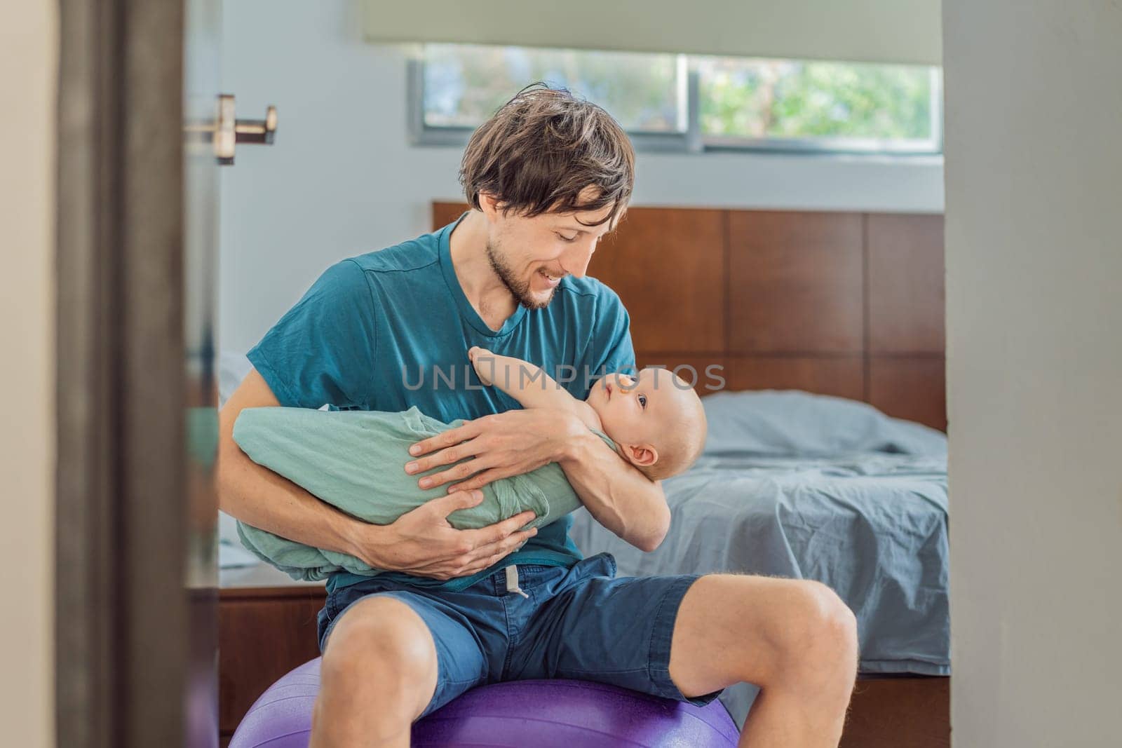 A father sits on a fitness ball in a cozy bedroom, gently rocking his baby wrapped in a soft muslin swaddle. A nurturing and soothing moment of fatherhood and care. Parenting, bonding, and comfort concept.