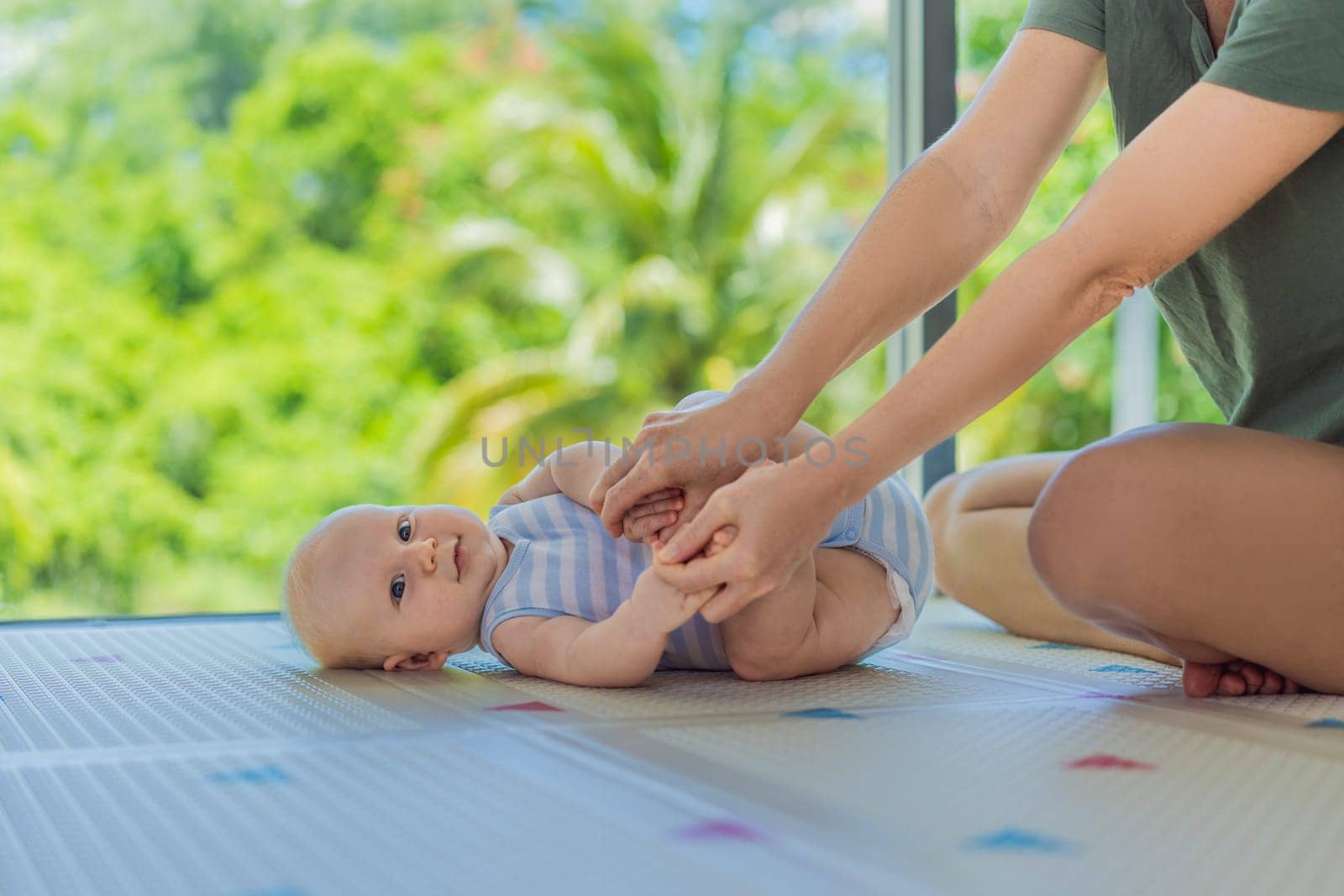 A mother practices baby gymnastics with her 3-month-old on a soft children's play mat. A joyful and nurturing moment focused on bonding, development, and care. Early childhood, fitness, and parenting concept.