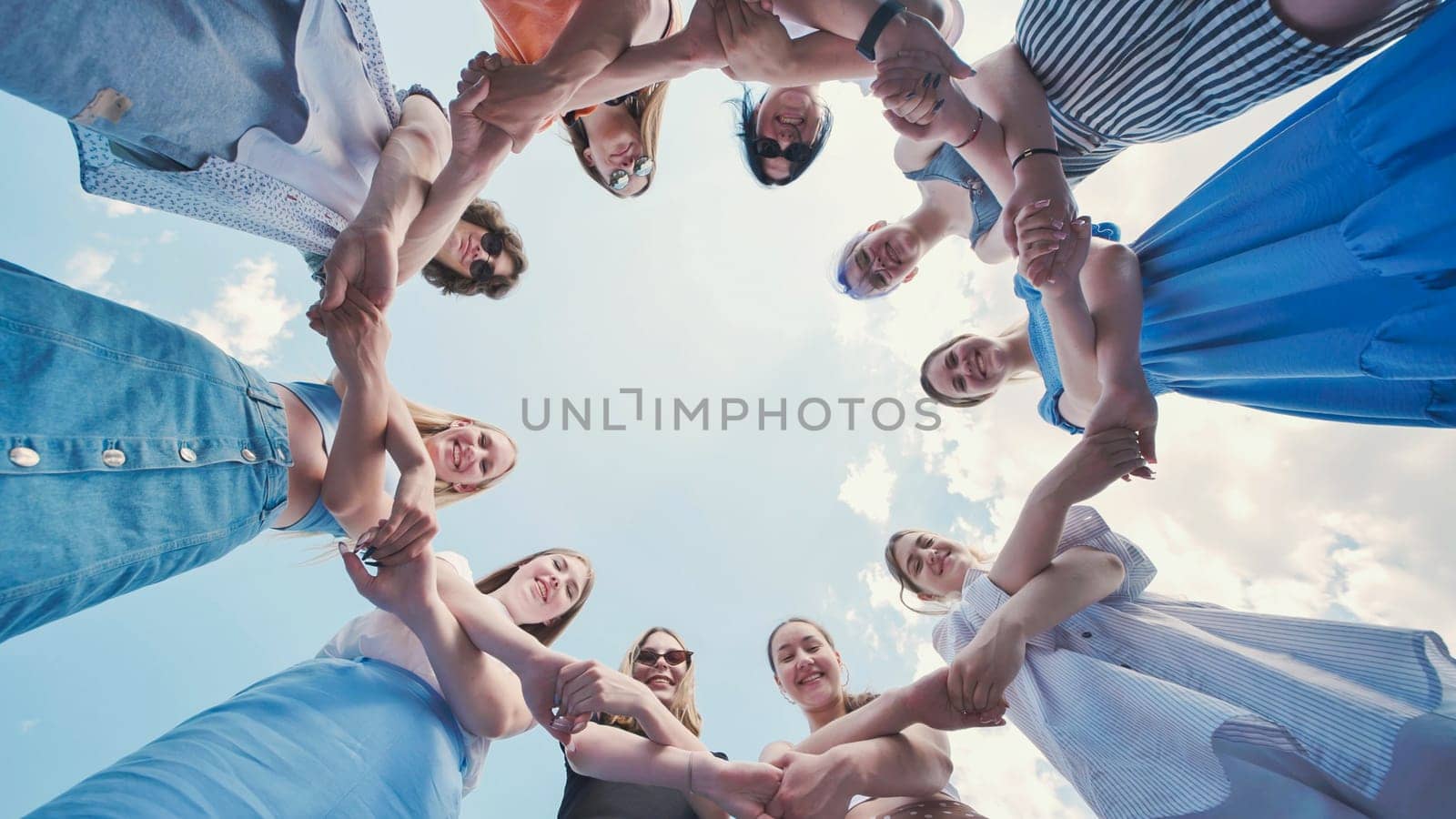 Group of school friends holding hands, forming a circle, and looking down at the camera against a cloudy sky, symbolizing unity and friendship