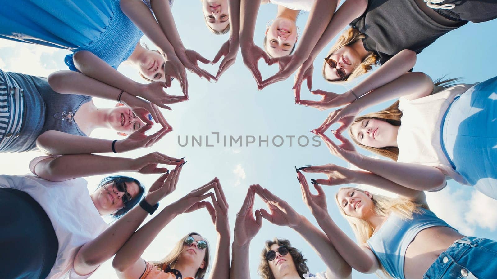 Group of school friends making heart shapes with their hands forming a star against a blue sky, symbolizing unity, friendship, and teamwork