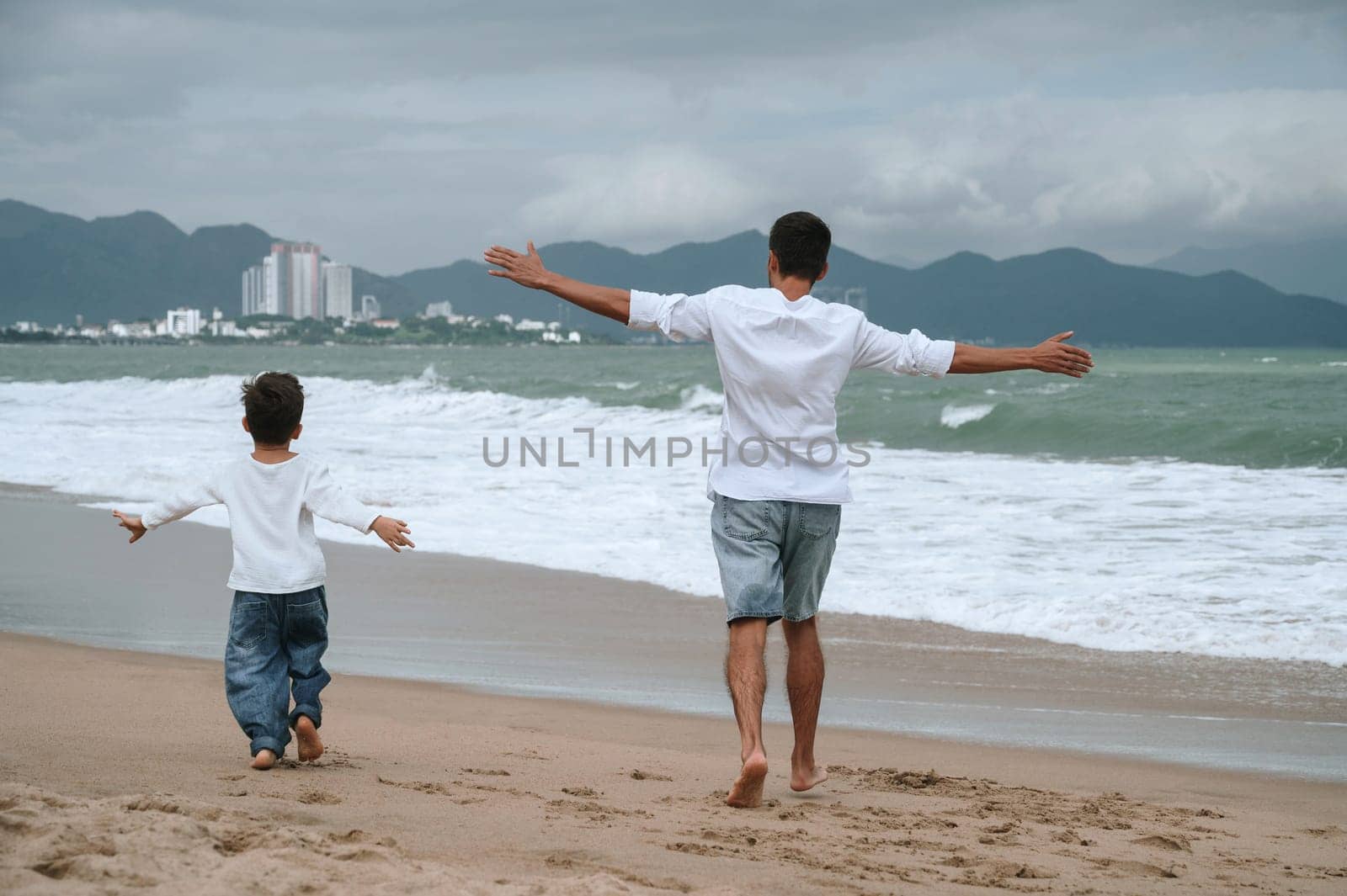back of happy father dad with a child son are walking along the beach by the sea on a summer vacation