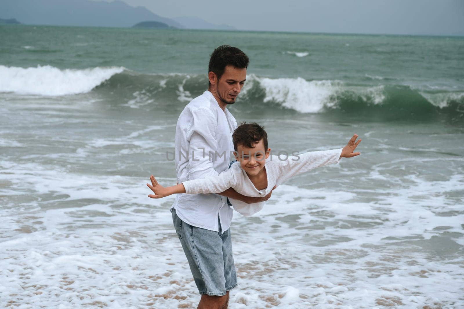 happy father dad with child boy son playing on the beach by the sea in summer on vacation