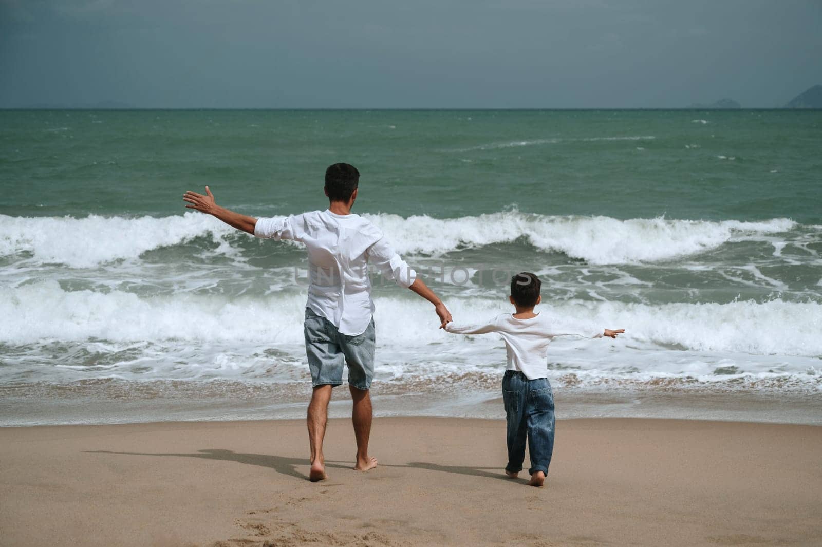 back of happy father dad with child boy son running along the beach by the sea in summer on vacation