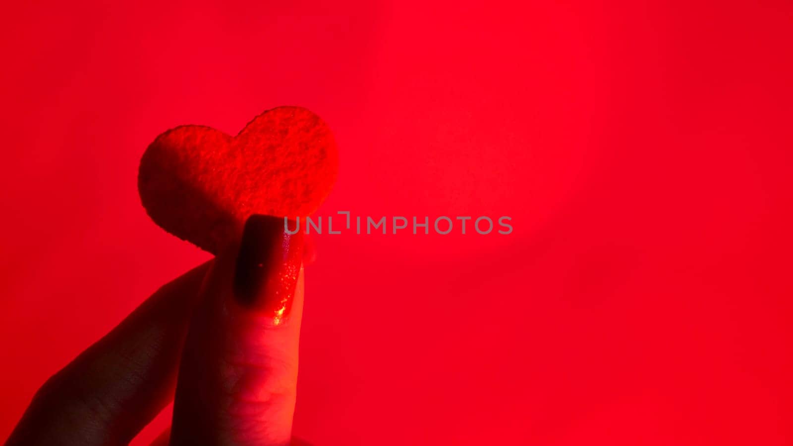 Woman Hands Attach a Decorative Red Heart of love Against a Neon Background for International Valentine's Day, February 14