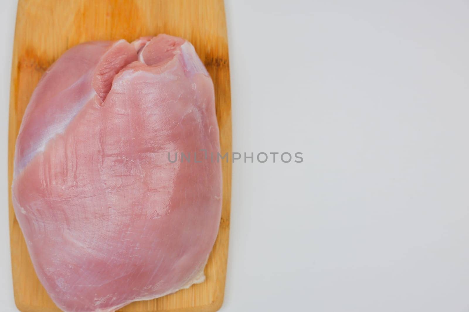 On a wooden cutting board lies a close-up piece of turkey meat on a white background with space for text. The concept of a diet menu, cooking. High quality photo