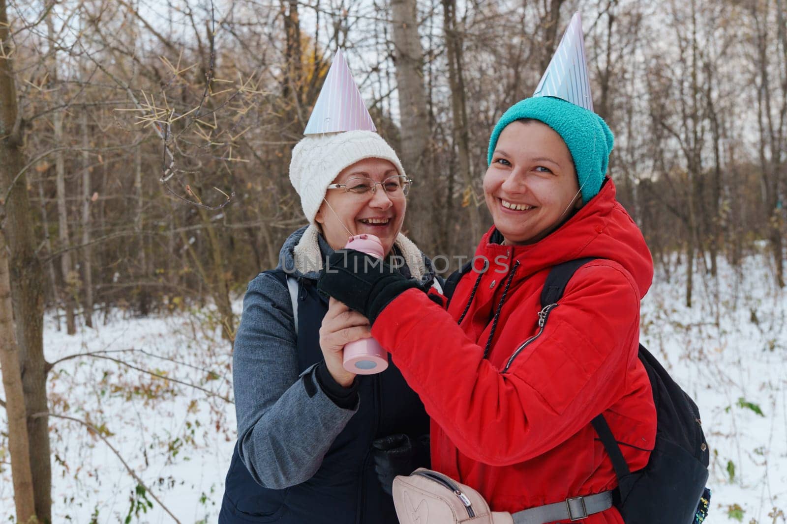 Two friends embrace the winter chill while hiking through a snowy forest, laughing and capturing the spirit of friendship