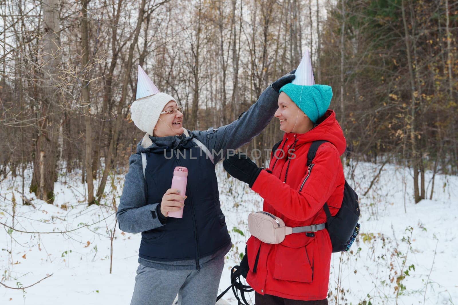 Two friends embrace the winter chill while hiking through a snowy forest, laughing and capturing the spirit of friendship