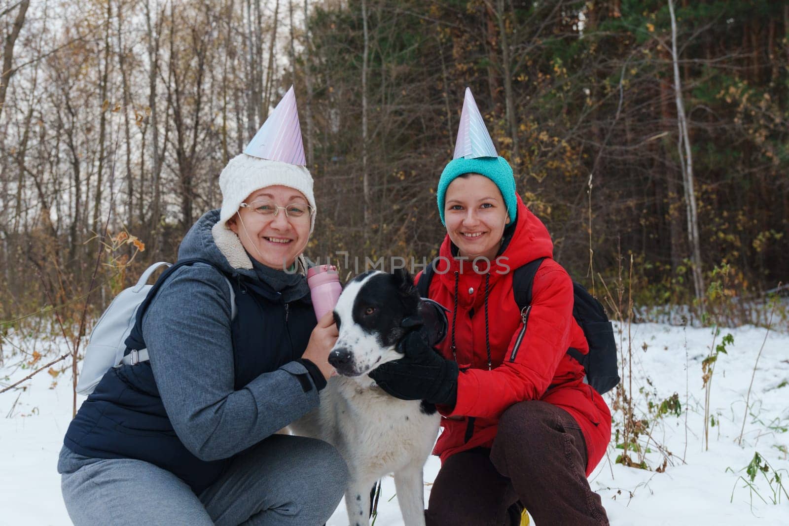 Celebrating in the snowy woods with friends and a loyal dog while wearing festive hats and enjoying a joyful winter day